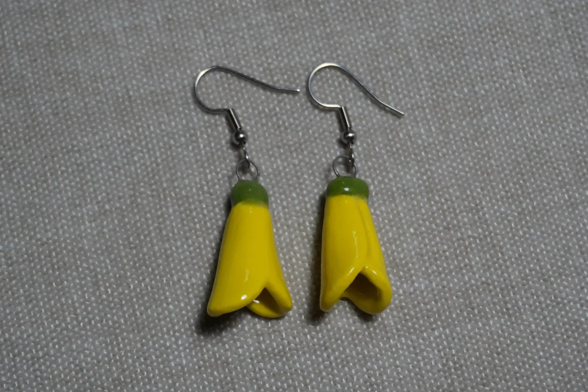 Ceramic pottery earrings featuring New Zealand yellow Kowhai flowers with shiny metal hooks, displayed on a neutral background.