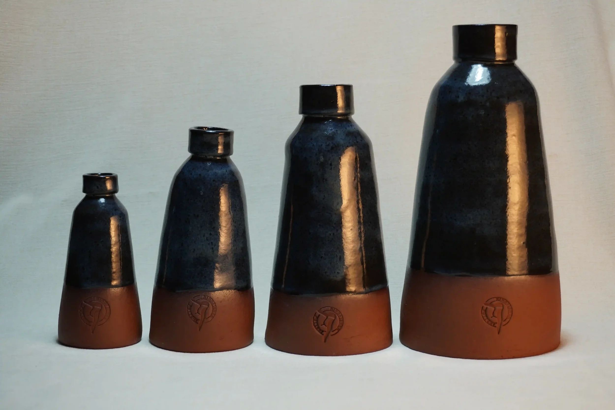 A set of four ceramic vases varying in size from small to large, with a glossy dark blue glazed top and a terracotta-colored base, displayed against a plain light background.