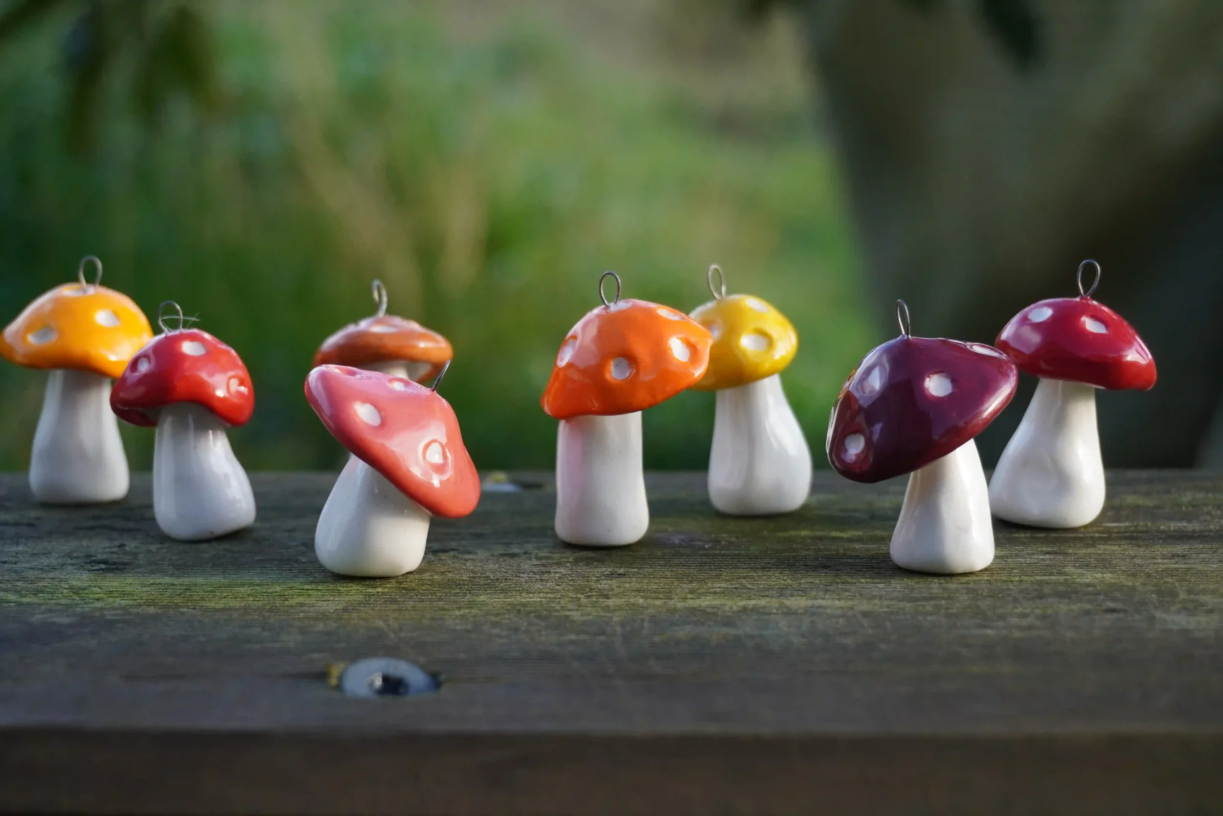 Colorful ceramic mushroom-shaped figurines arranged in a line on a wooden surface with a blurred green background.