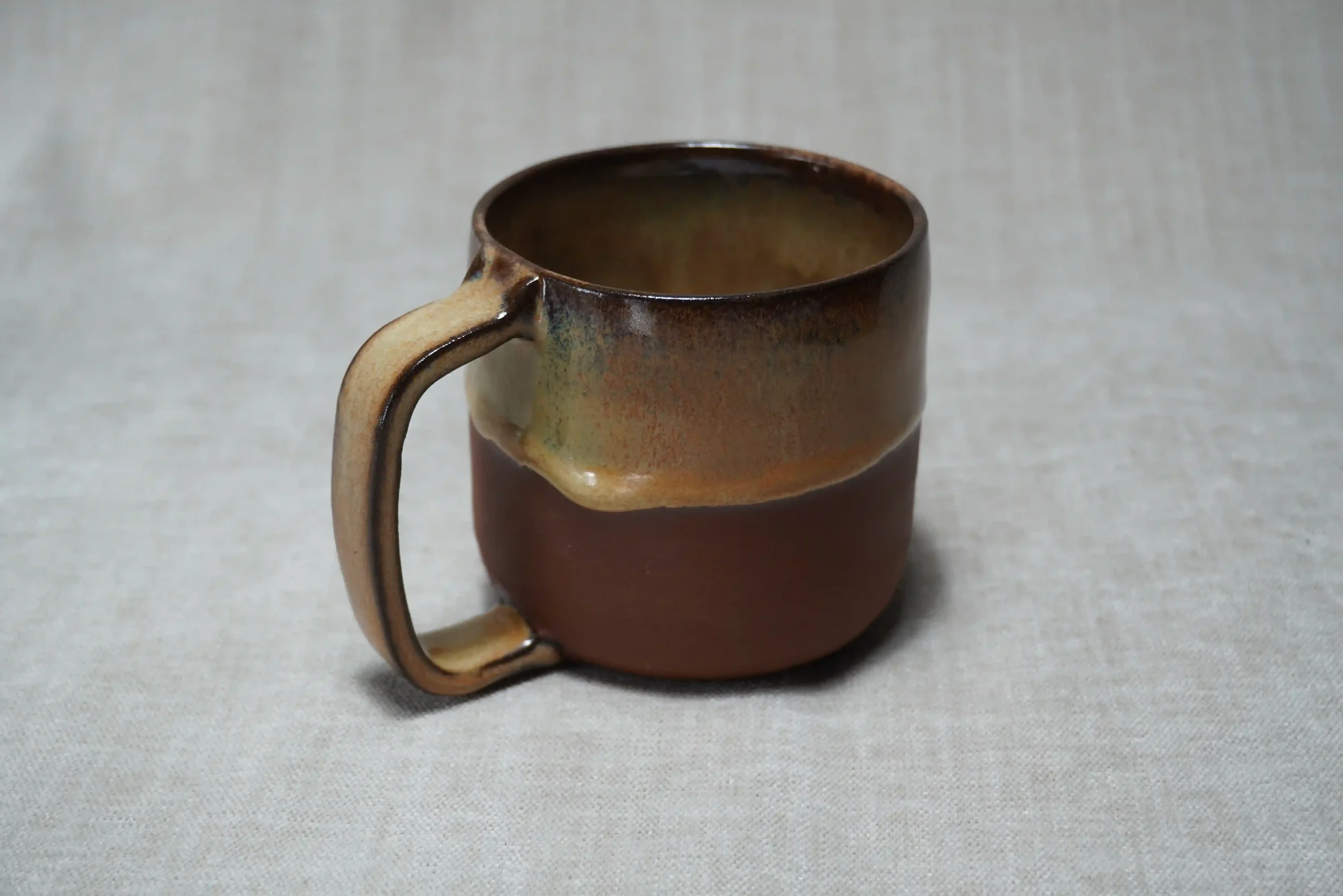 A ceramic mug with a brown and honey-coloured gradient glaze, placed on a light-colored textured surface.