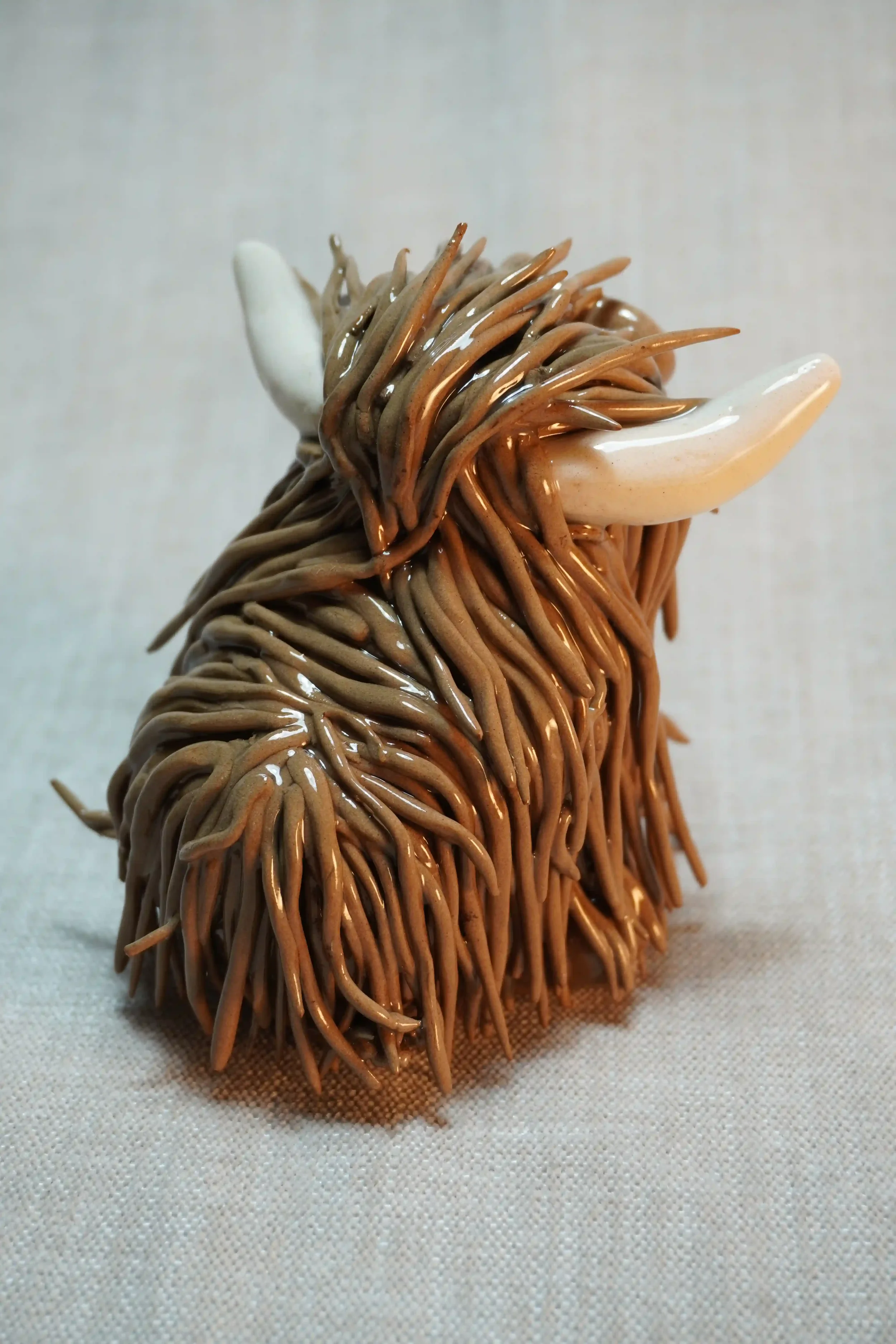 Rear view of a medium brown handmade ceramic ornament of a Highland Cow with beige horns.