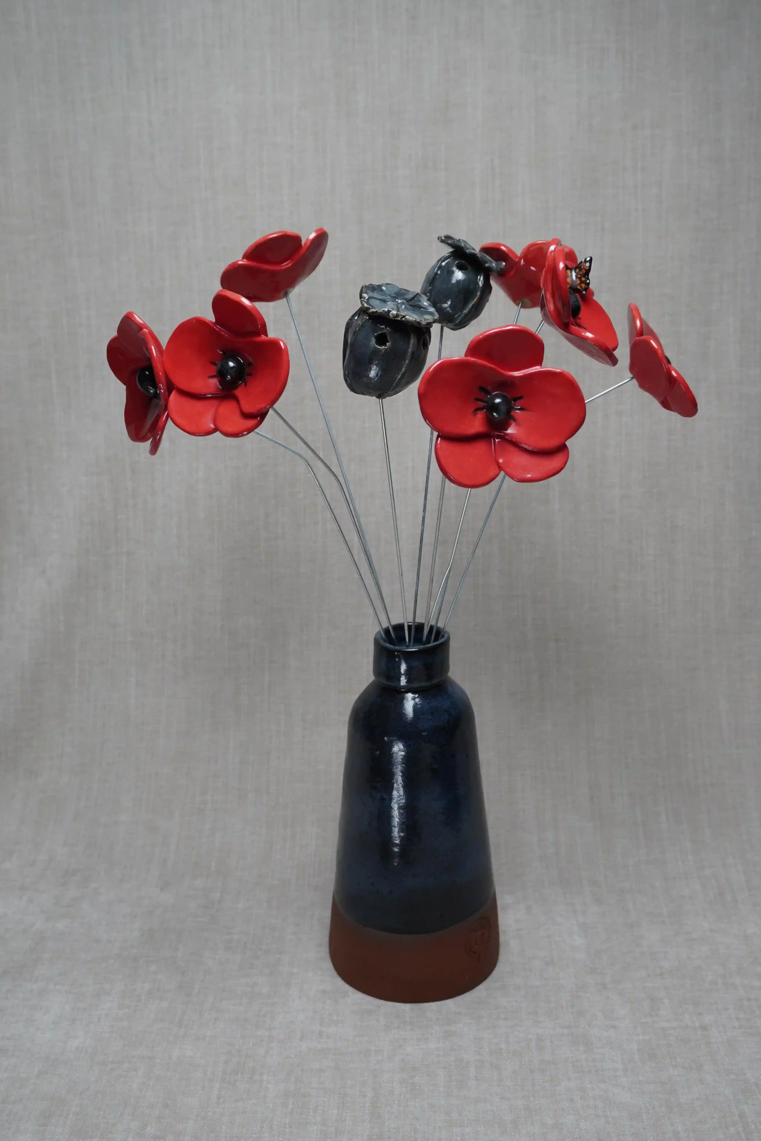 A decorative bouquet of Pottery poppies in a tall dark ceramic vase set against a gray background.