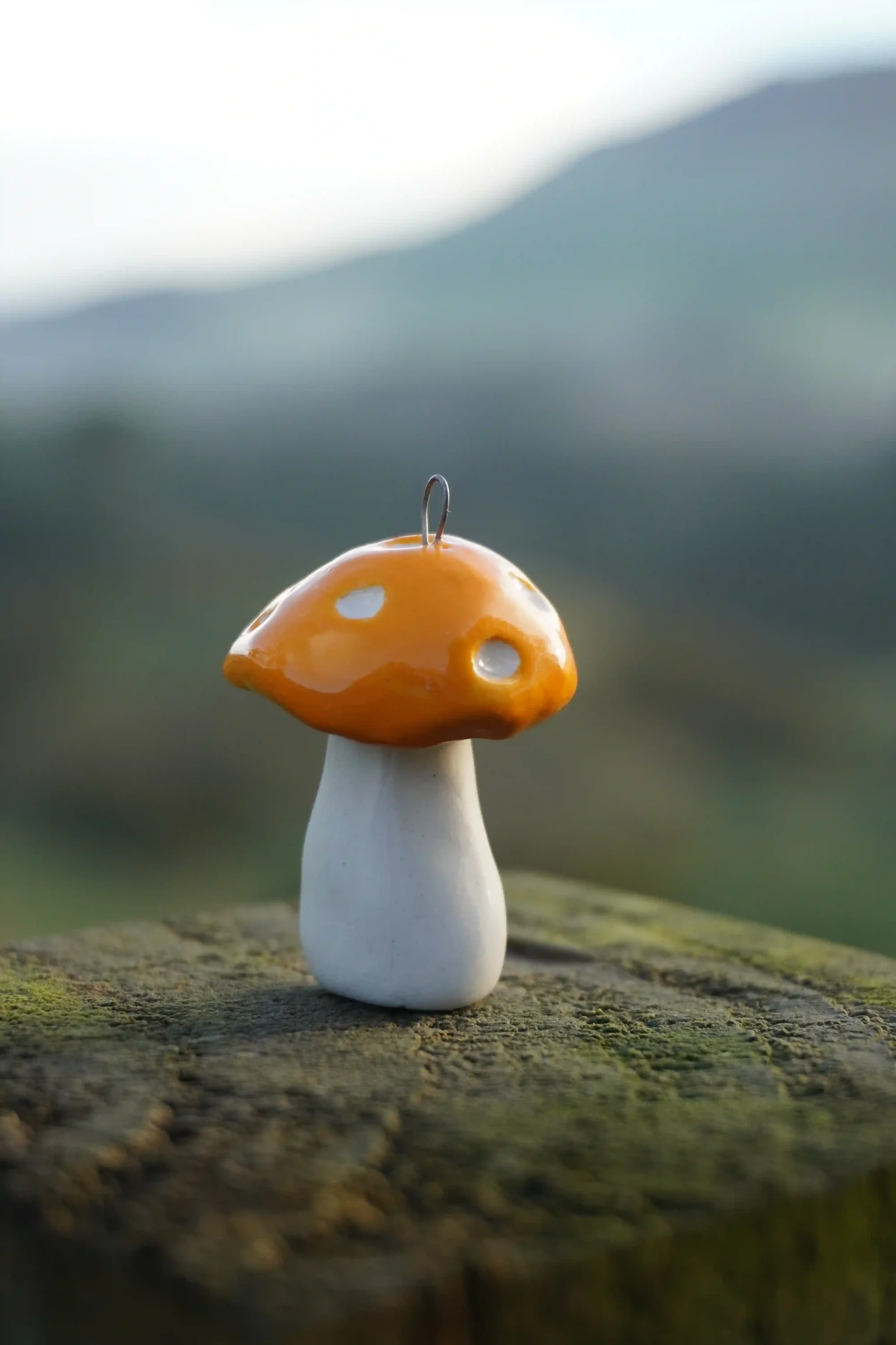 A decorative ceramic mushroom figurine with a white stem and yellow-orange cap with white spots, placed on a rough wooden surface outdoors.