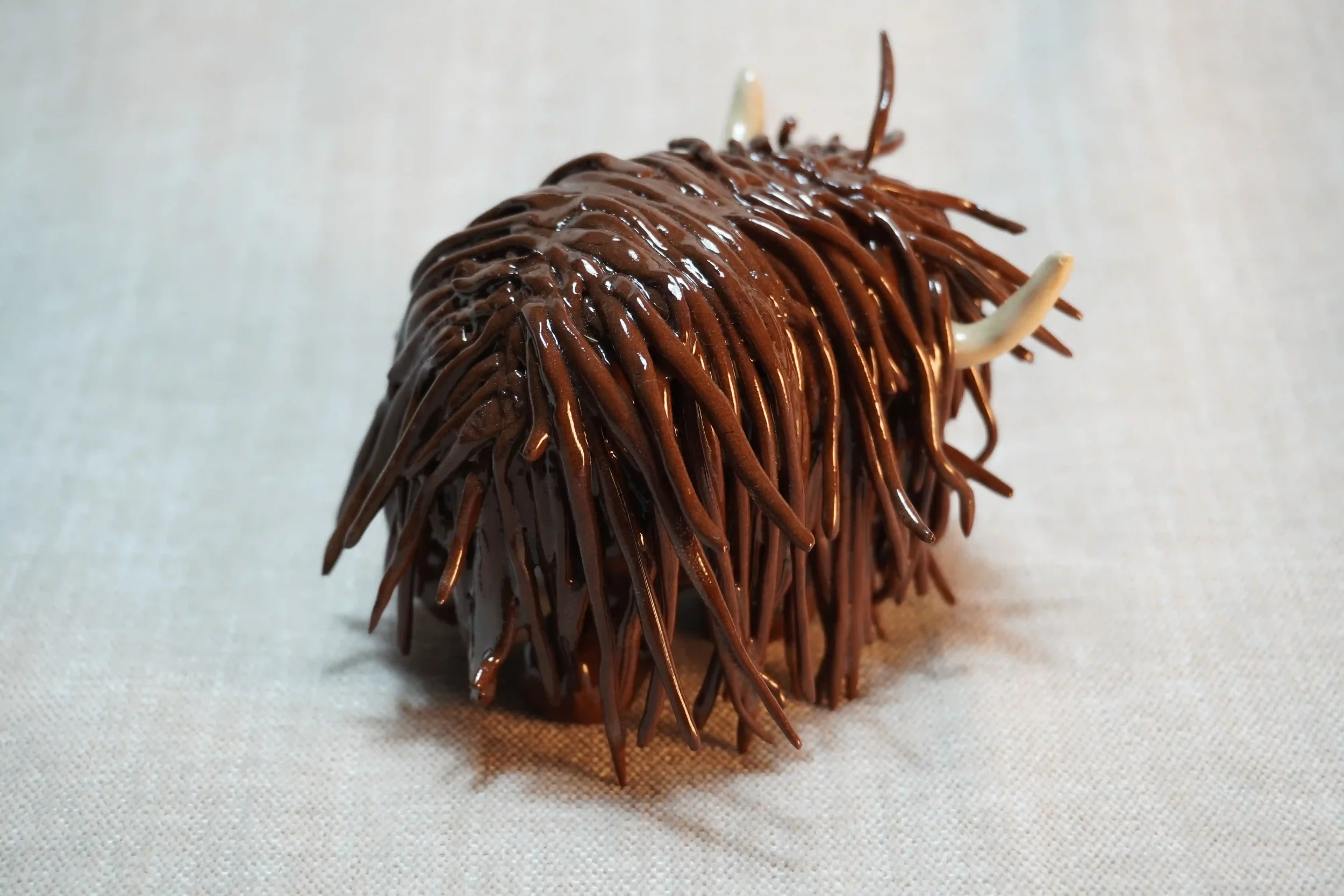 	
Quarter rear view of a ceramic sculpture of a Highland Cow ornament with dark brown-coloured hair and beige horns.