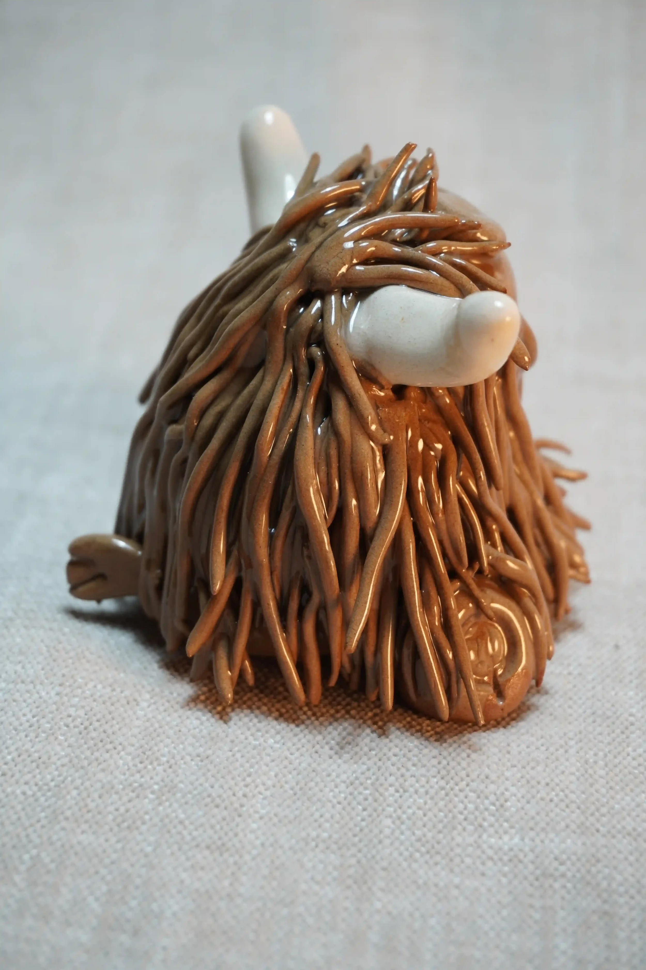 Side view of a handmade ceramic Highland Cow ornament with rich chocolate brown-coloured hair and beige horns.