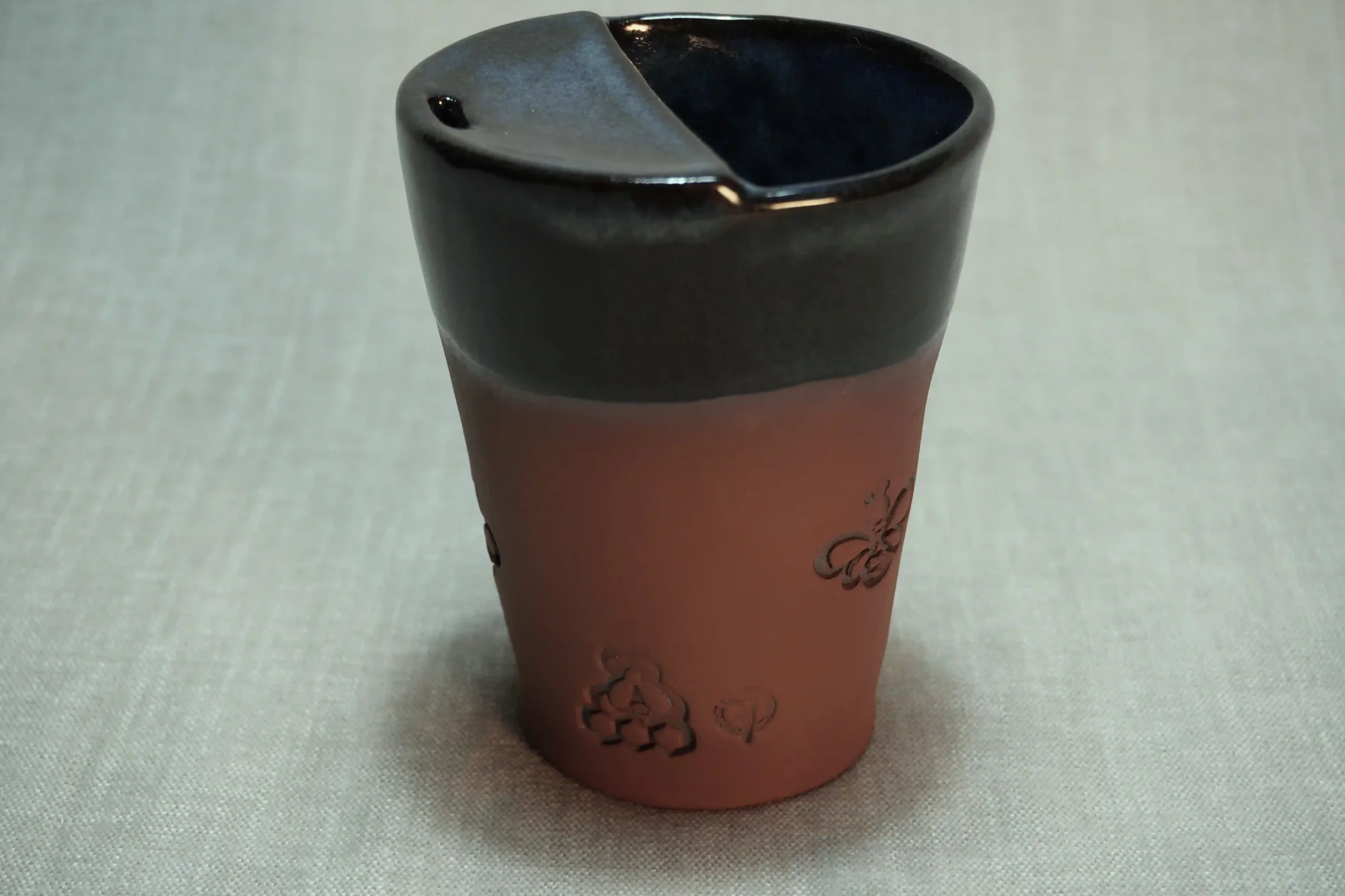A ceramic mug with a matte surface, decorated with black floral designs, and dark glaze on the interior.