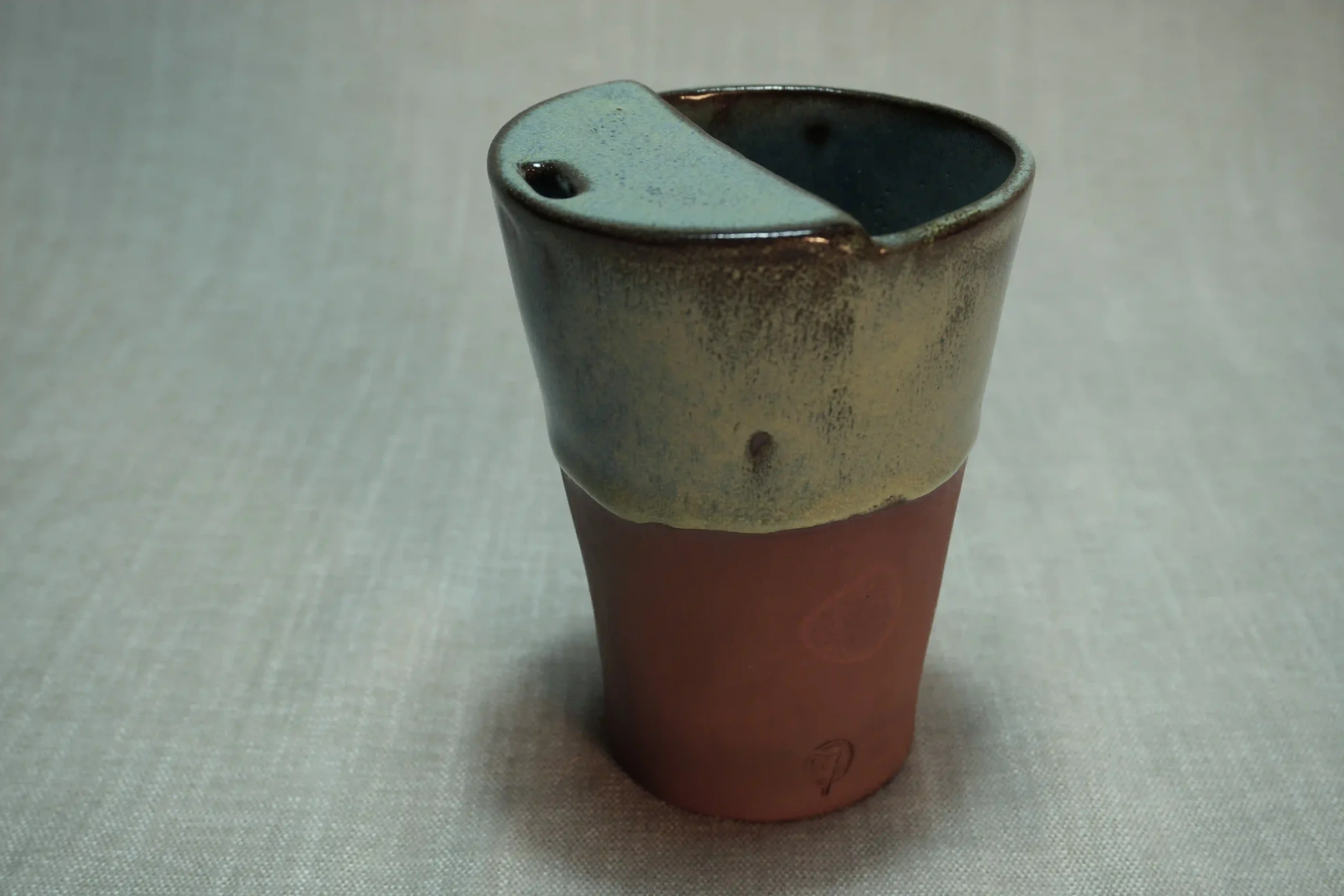 A ceramic cup with a half-black, half-cream glaze sitting on a light-colored surface.