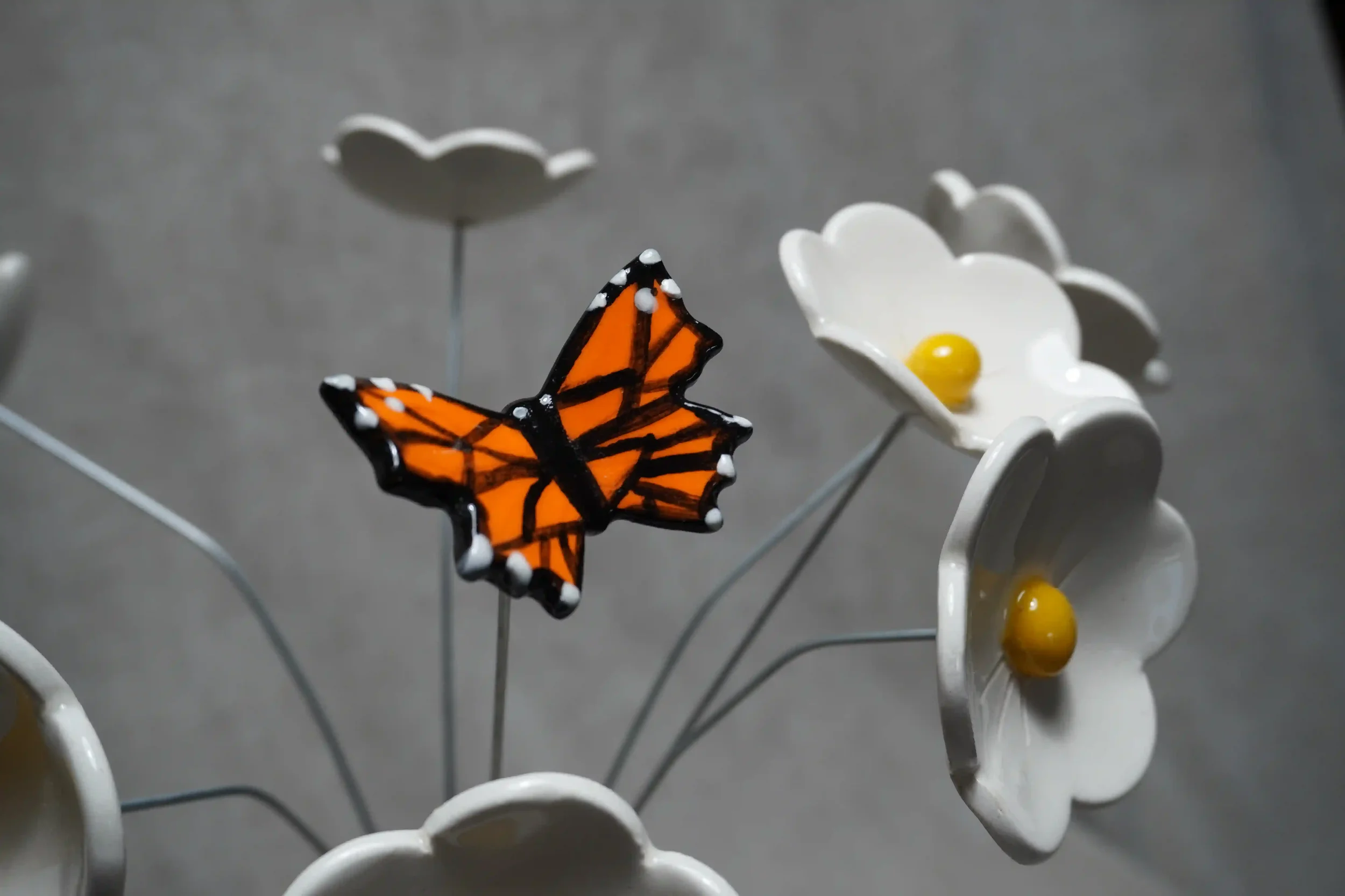 Decorative handmade white ceramic Daisy flowers with a yellow center and metal wire stems, featuring a ceramic black and orange Monarch butterfly ornament.