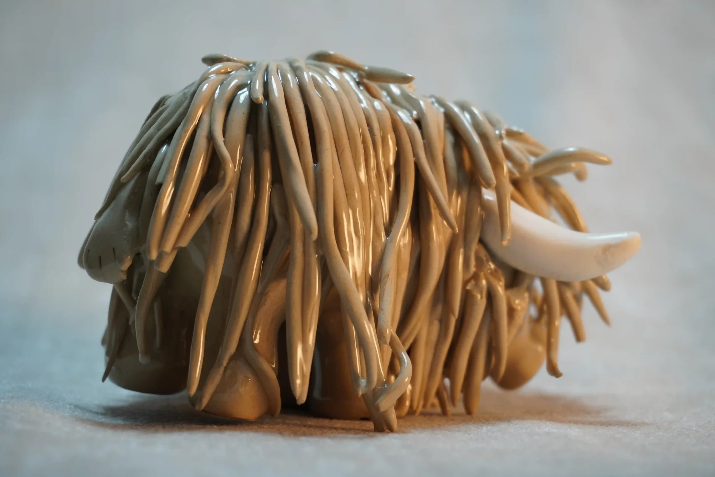 Side view of a handmade ceramic Highland Cow ornament with brown-coloured hair and beige horns.