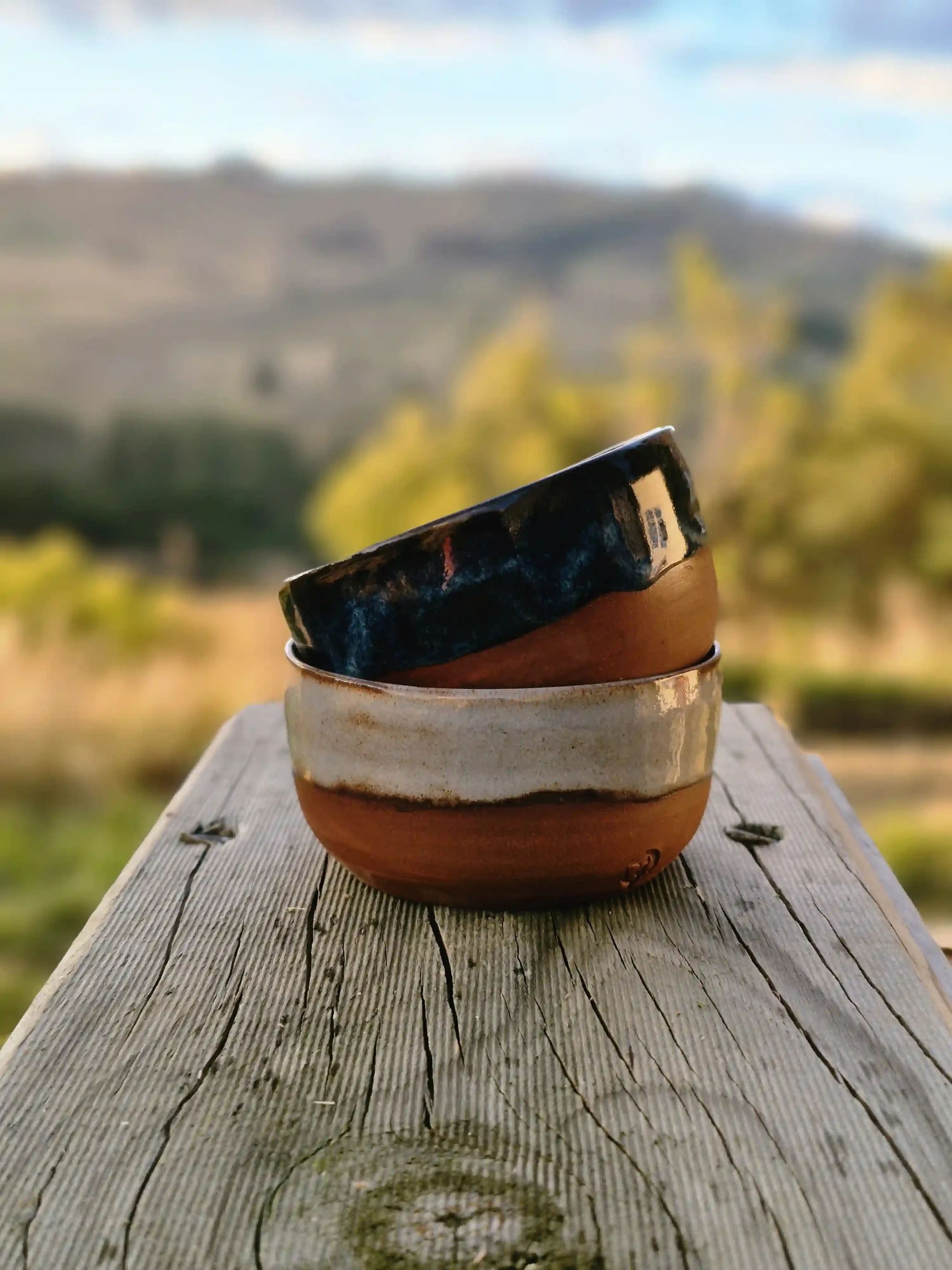 Stacked ceramic bowls on a wooden surface with blurred outdoor landscape in the background.
