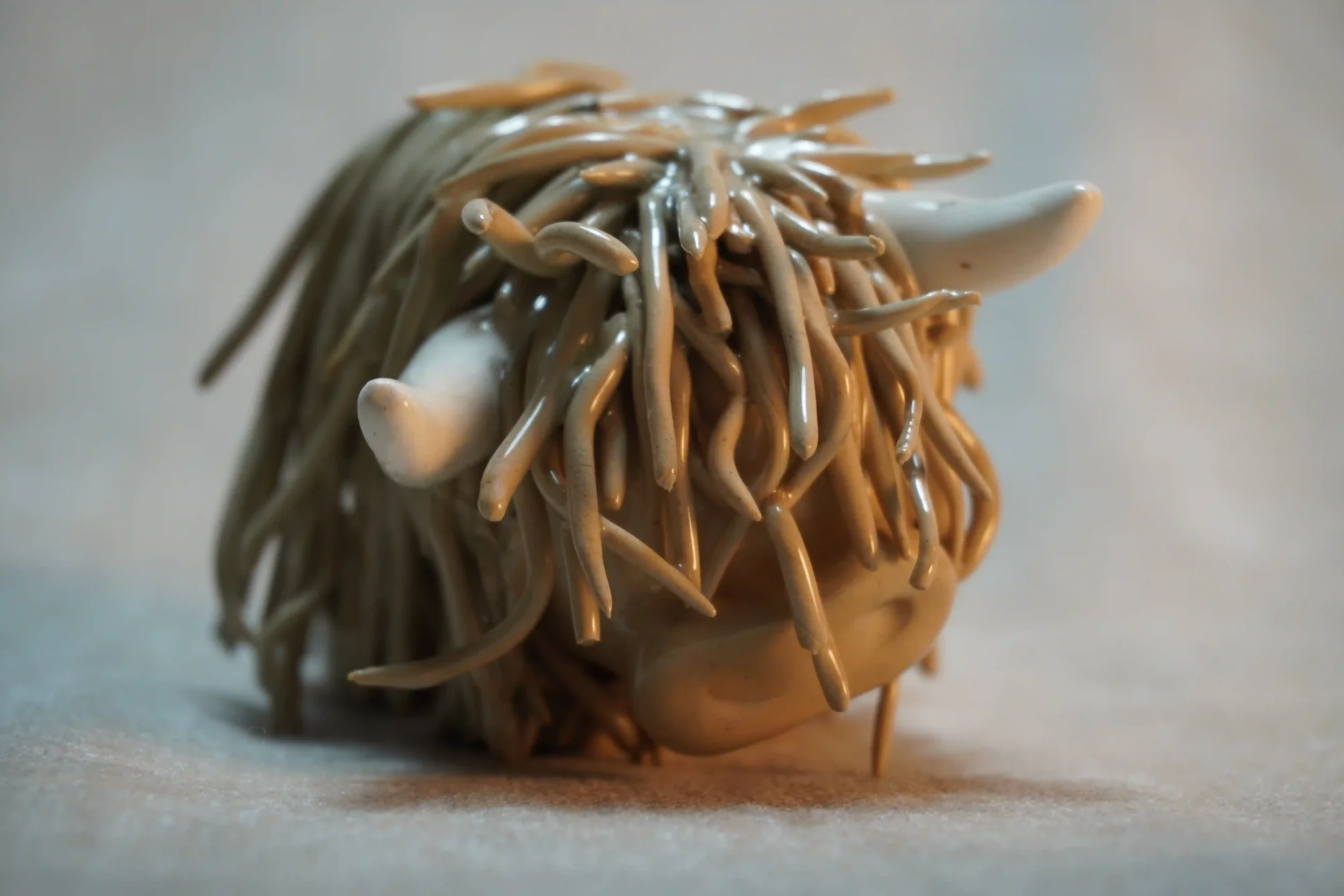 Close-up front view of a ceramic sculpture of a Highland Cow ornament with brown-coloured hair and beige horns.