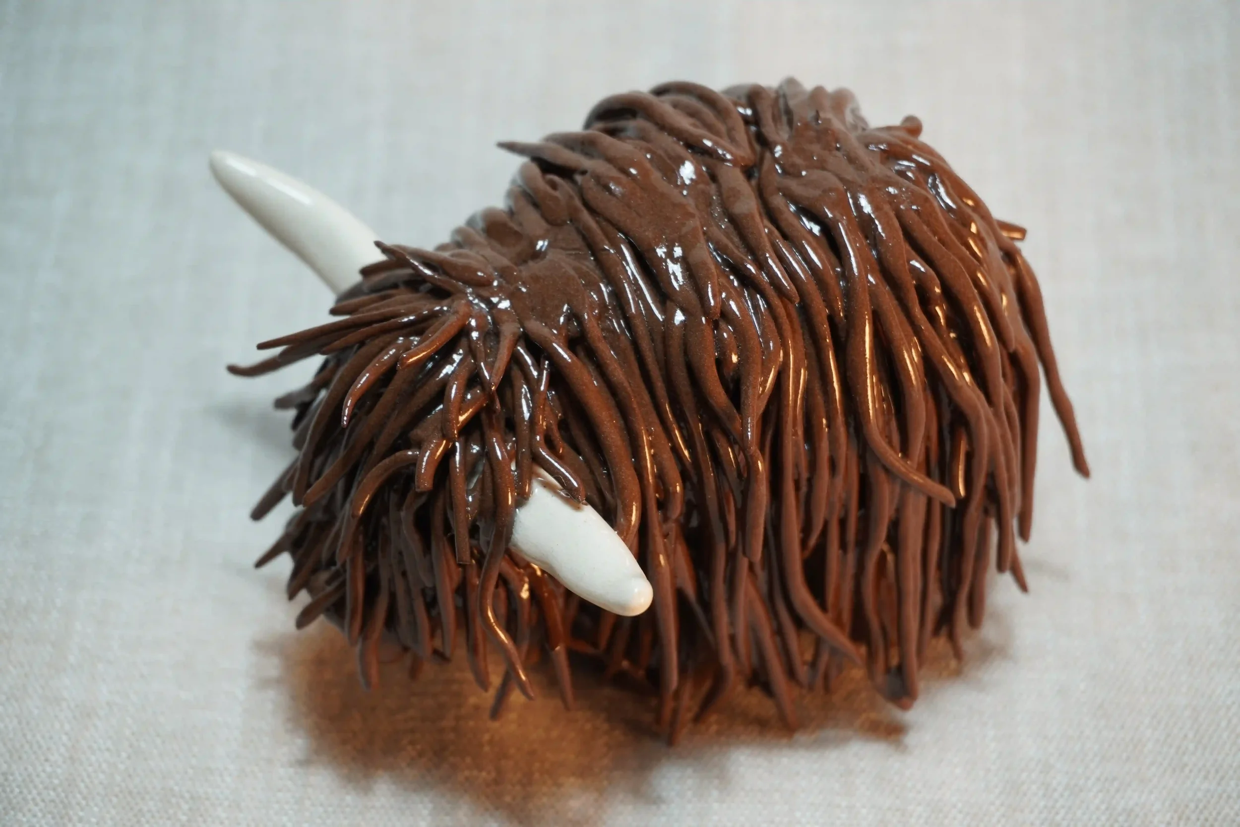 	
Quarter front view of a handmade pottery ceramic sculpture of a Highland Cow ornament with deep brown-coloured hair and beige horns.