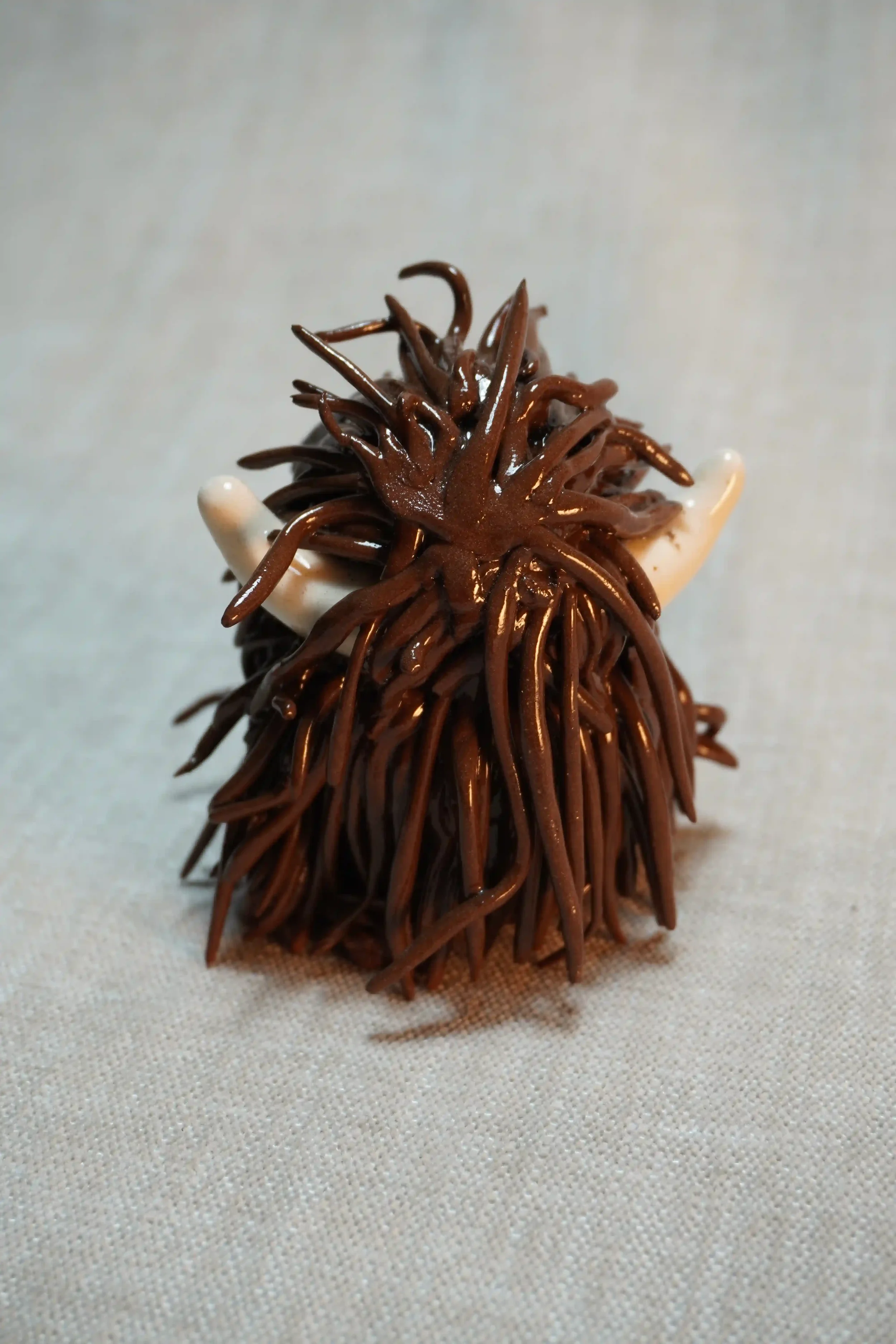 	
Rear view of a ceramic sculpture of a Highland Cow ornament with rich dark brown-coloured hair and beige horns.