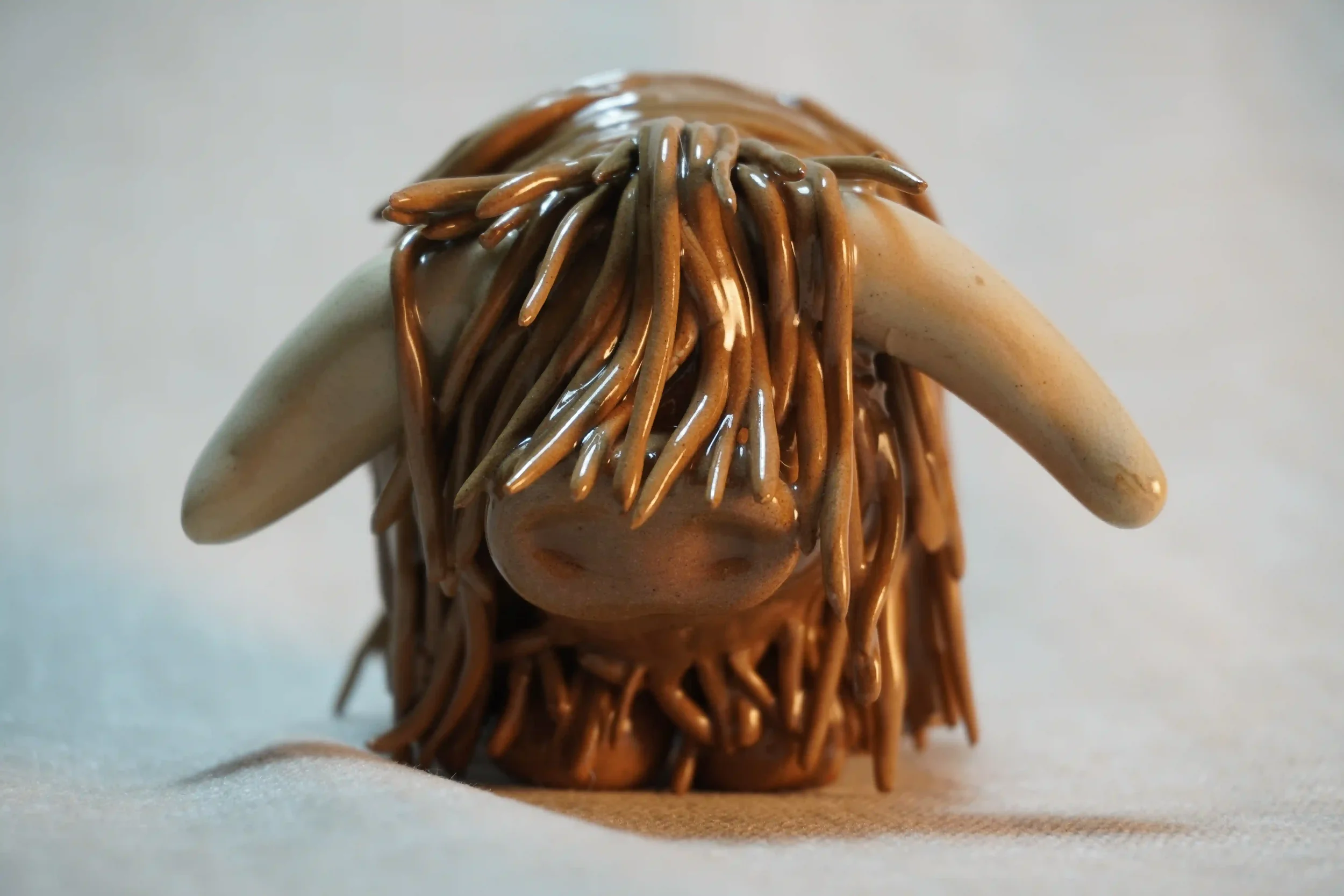 Frontal view of a cute ceramic Highland Cow ornament made by hand in a milk chocolate colour with beige horns.