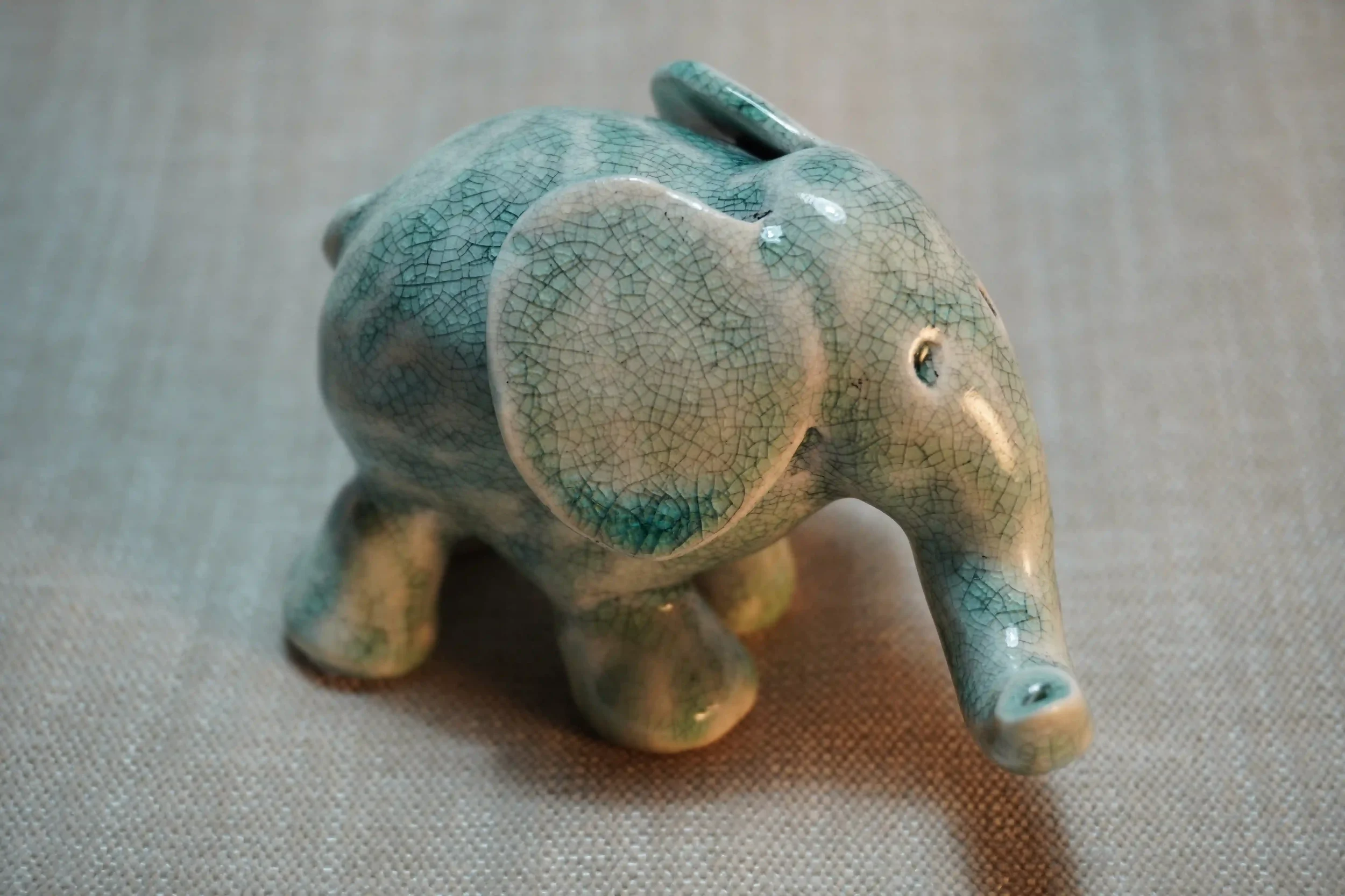 A handmade ceramic elephant figurine with a crackle glaze pattern in shades of blue, placed on a textured surface.
