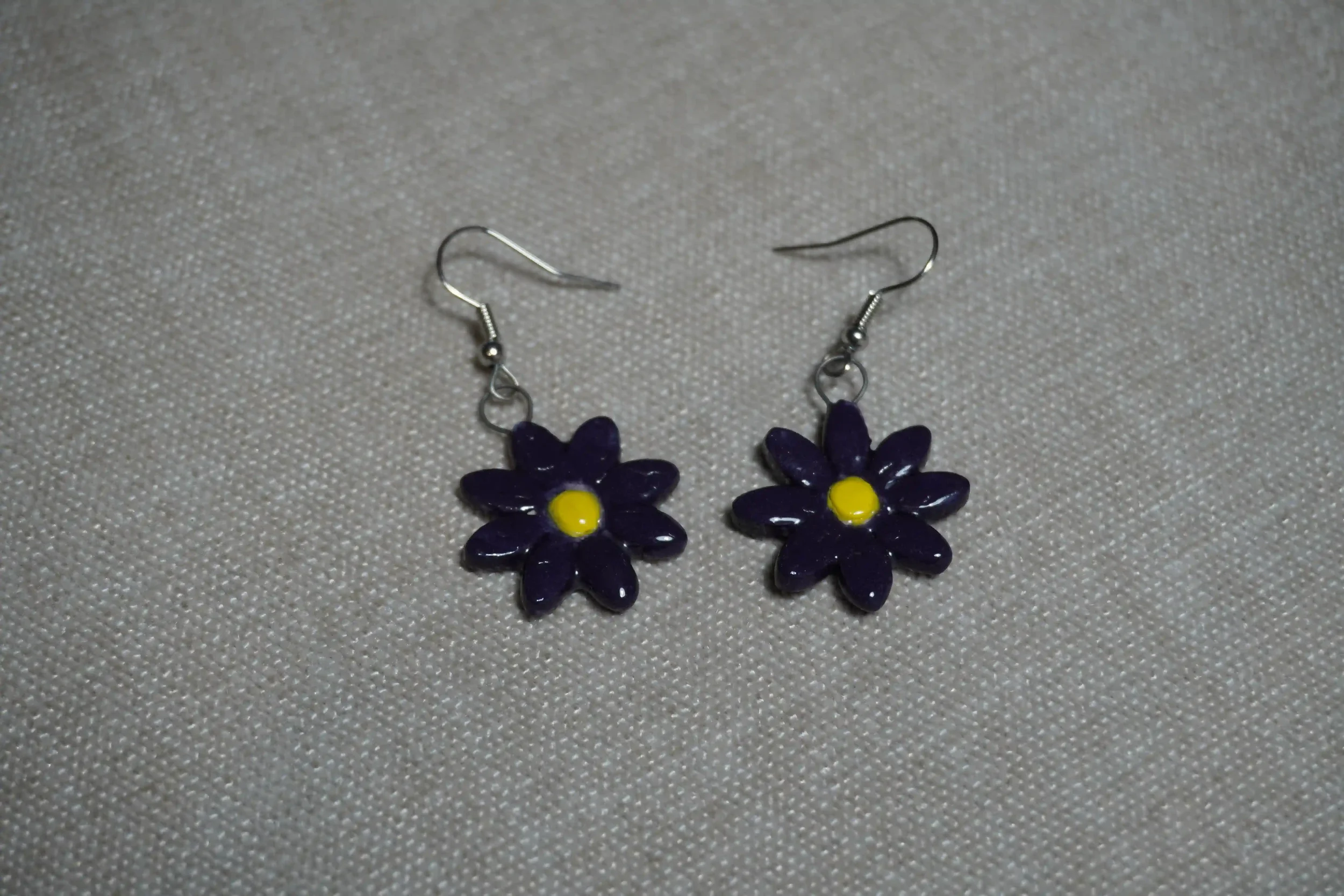 Pair of earrings with purple flower-shaped pendants with yellow centers on a textured grey background.