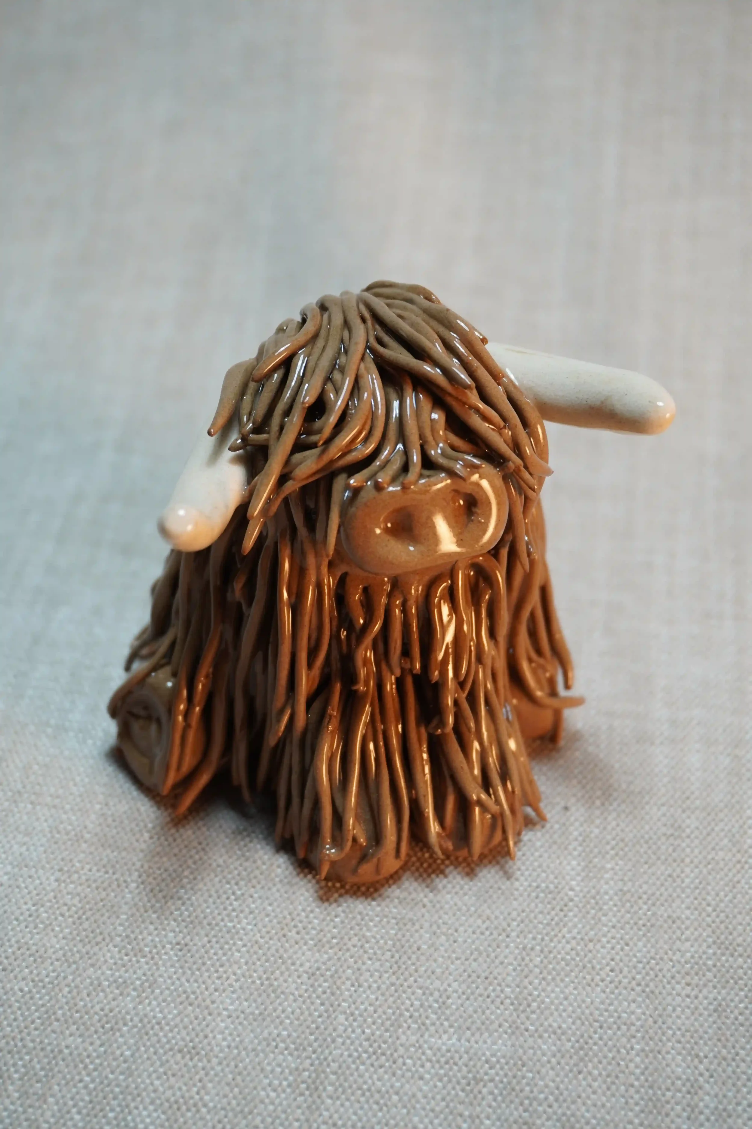 Front view of a ceramic sculpture of a Highland Cow ornament with rich chocolate brown-coloured hair and beige horns.