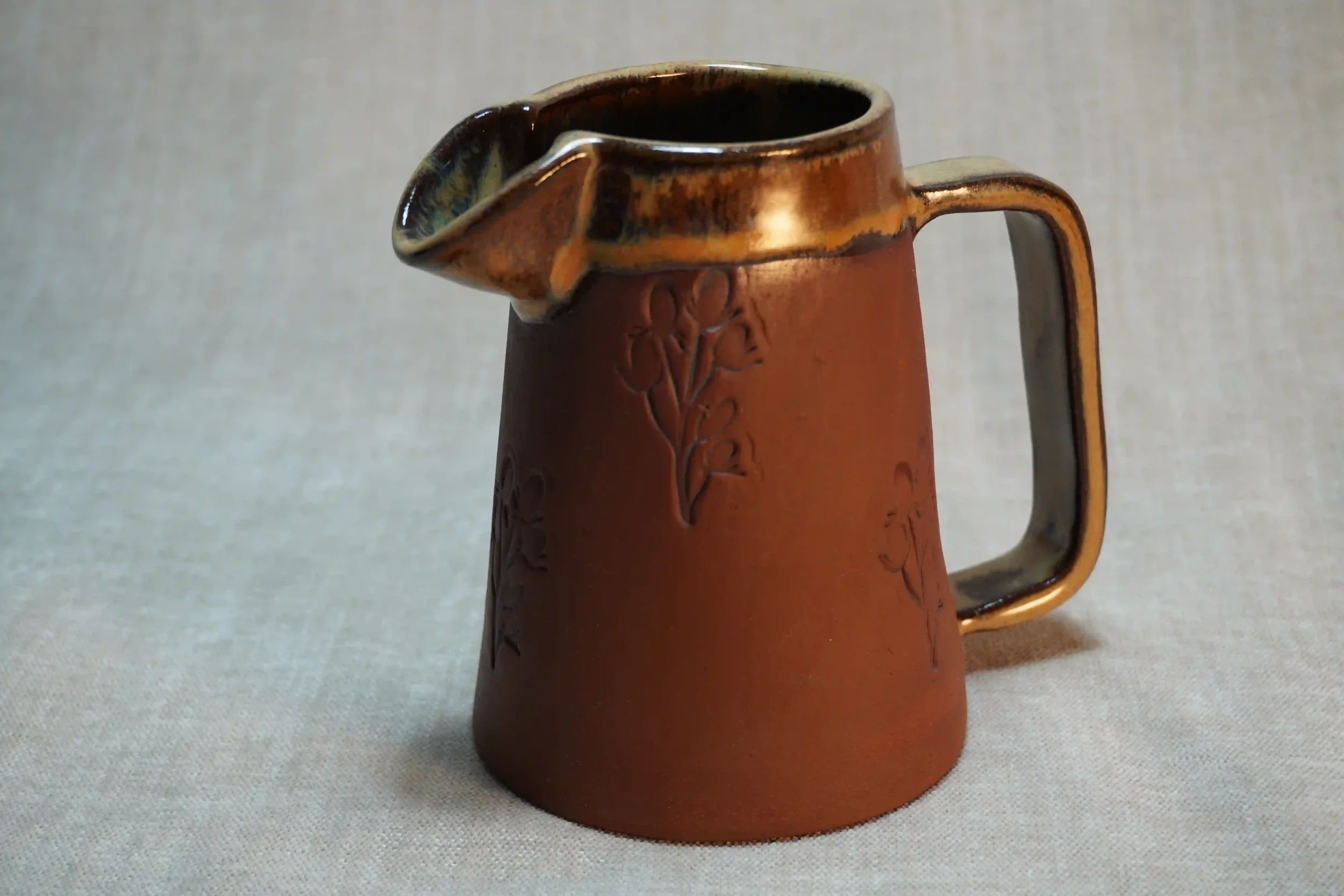 Handmade pottery ceramic pitcher (jug) with a handle, honey-coloured glaze, decorated with floral patterns