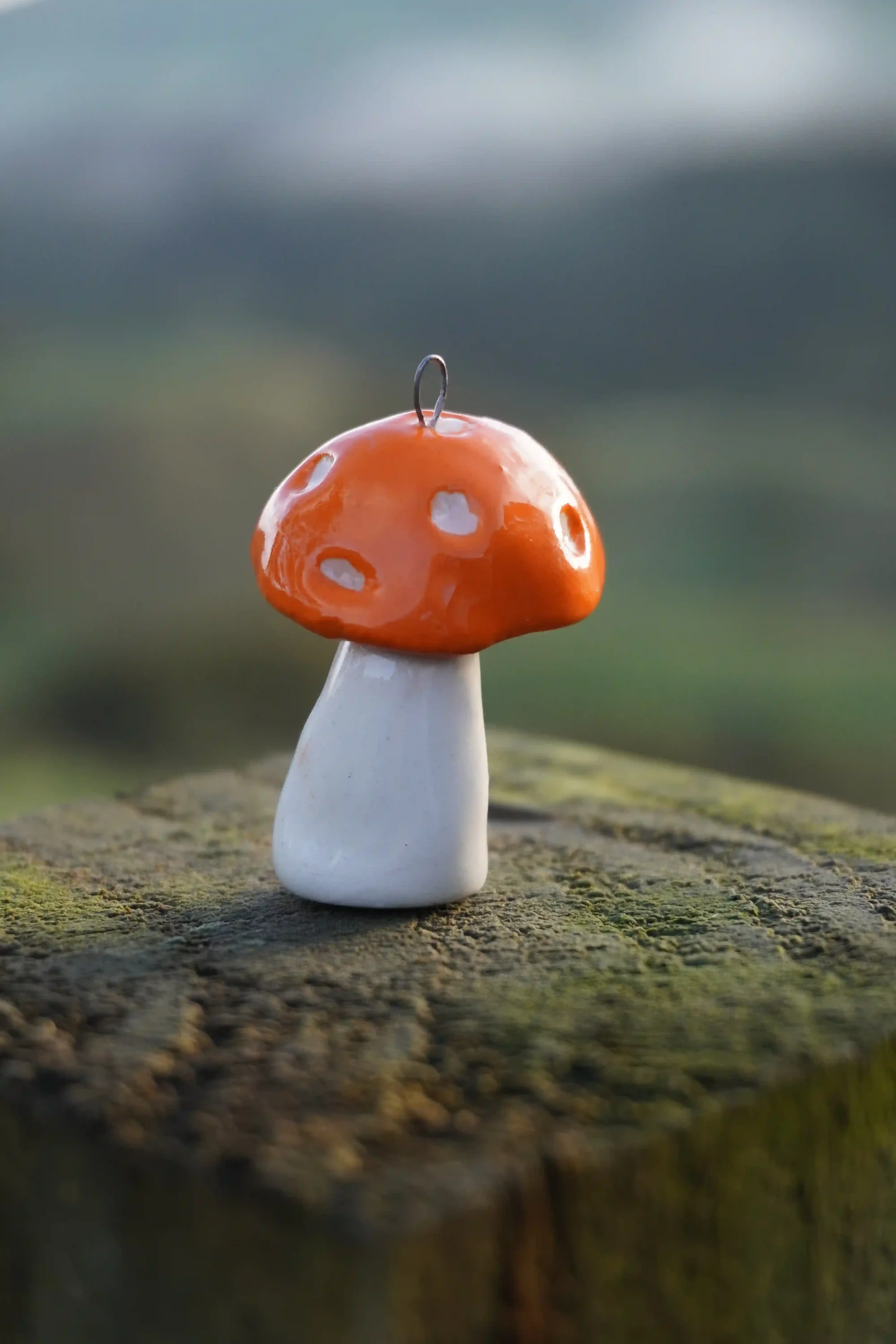 Close-up of a small, orange ceramic mushroom with white spots on a green mossy surface, with a blurred natural background.