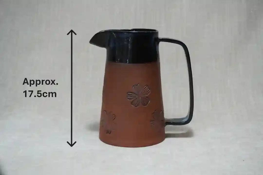 Brown pottery terracotta pitcher (jug) with black glaze upper and handle, decorated with floral motif, height approximately 17.5 centimeters.