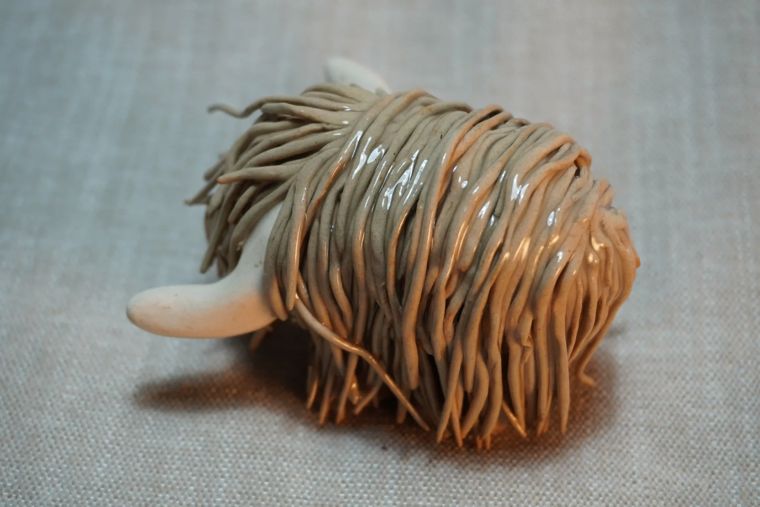 Side view of a handmade pottery ceramic sculpture of a Highland Cow ornament with light brown-coloured hair and beige horns.