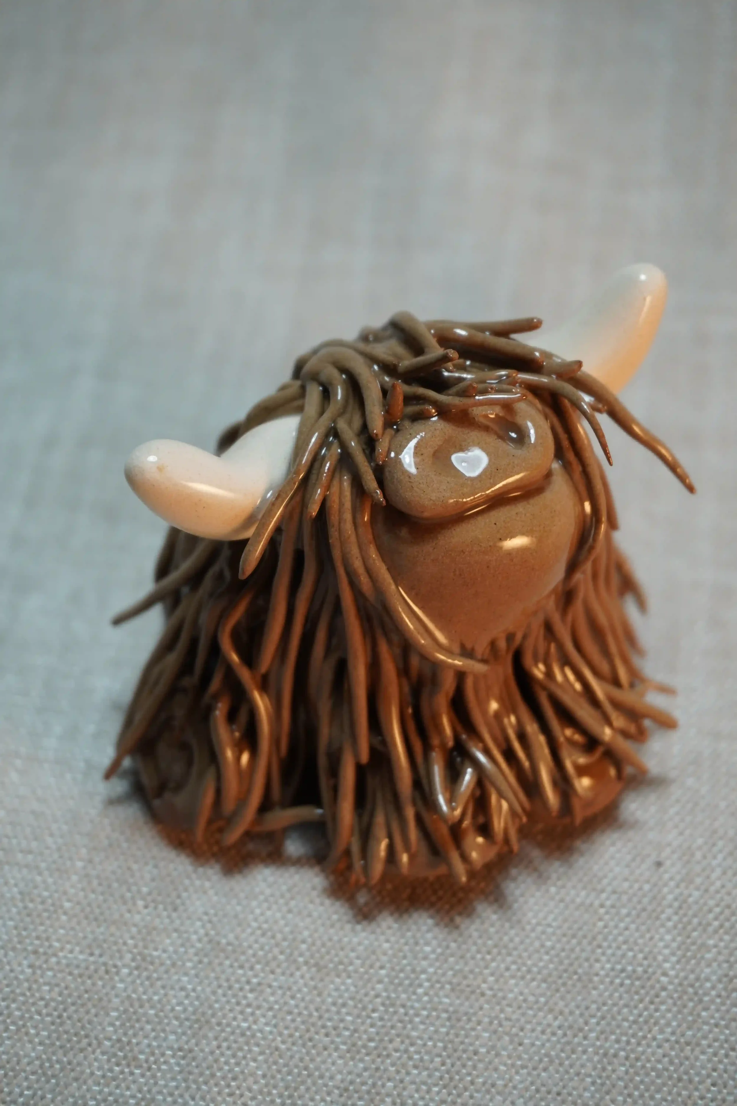 Quarter front view of a handmade ceramic Highland Cow ornament with rich chocolate brown-coloured hair and beige horns.