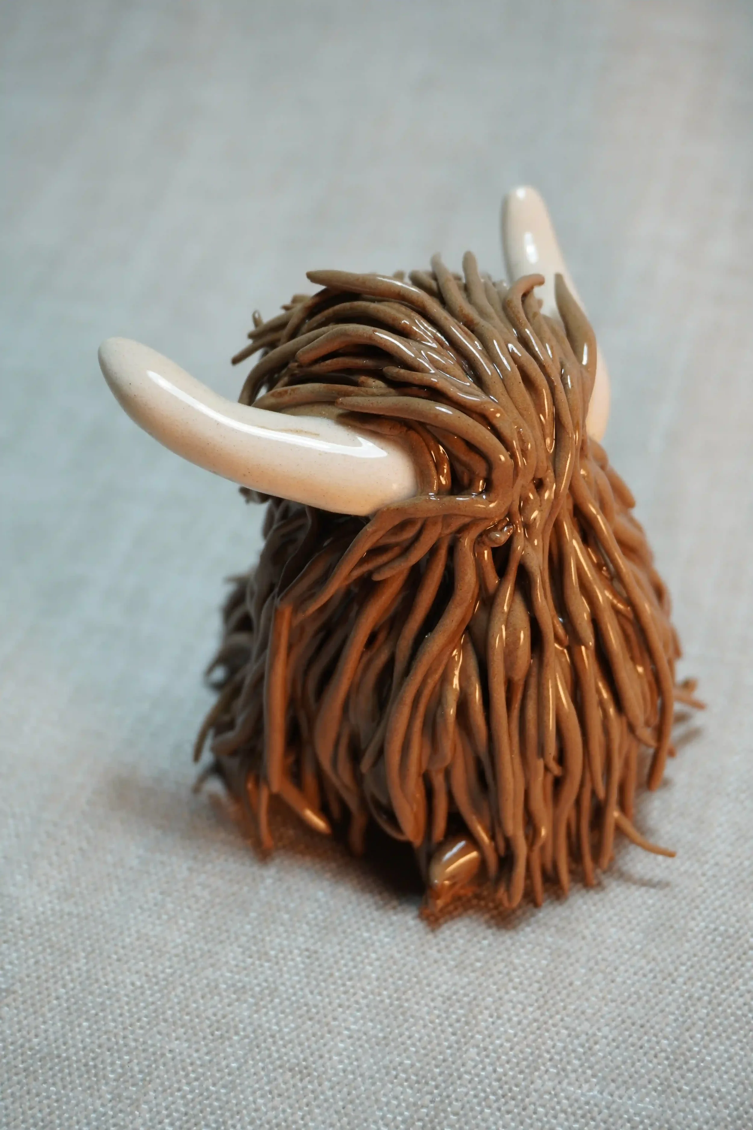 Side view of a ceramic sculpture of a Highland Cow ornament with rich chocolate brown-coloured hair and beige horns.