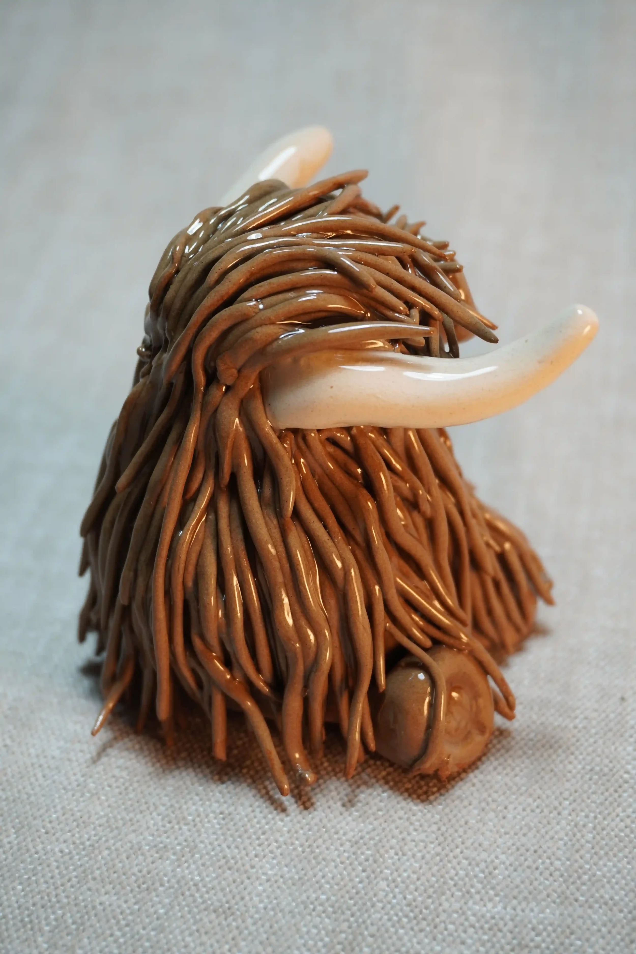 Front view of a ceramic sculpture of a Highland Cow ornament with rich chocolate brown-coloured hair and beige horns.