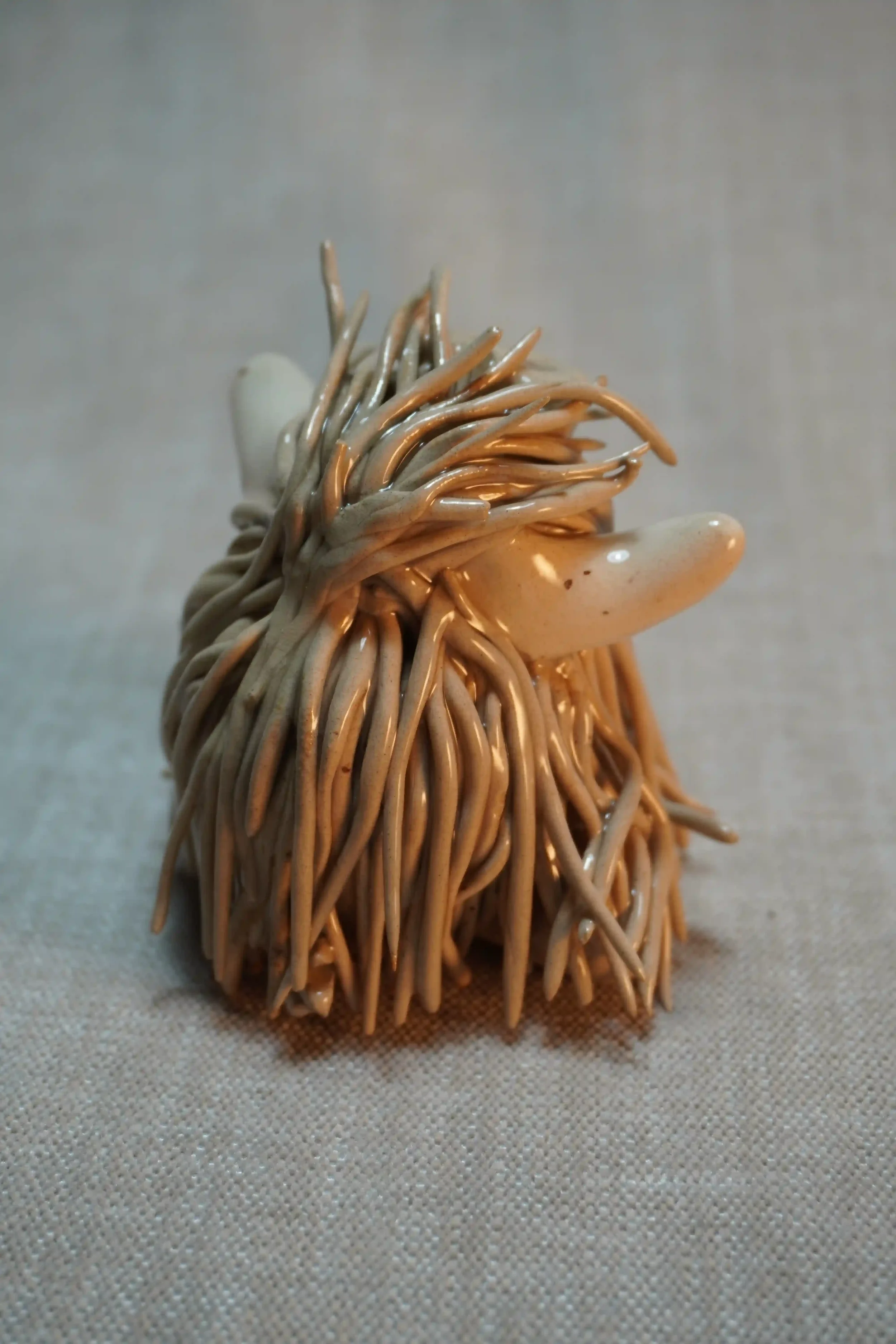 Rear view of a handmade ceramic sculpture of a Highland Cow ornament with light brown-coloured hair and beige horns.