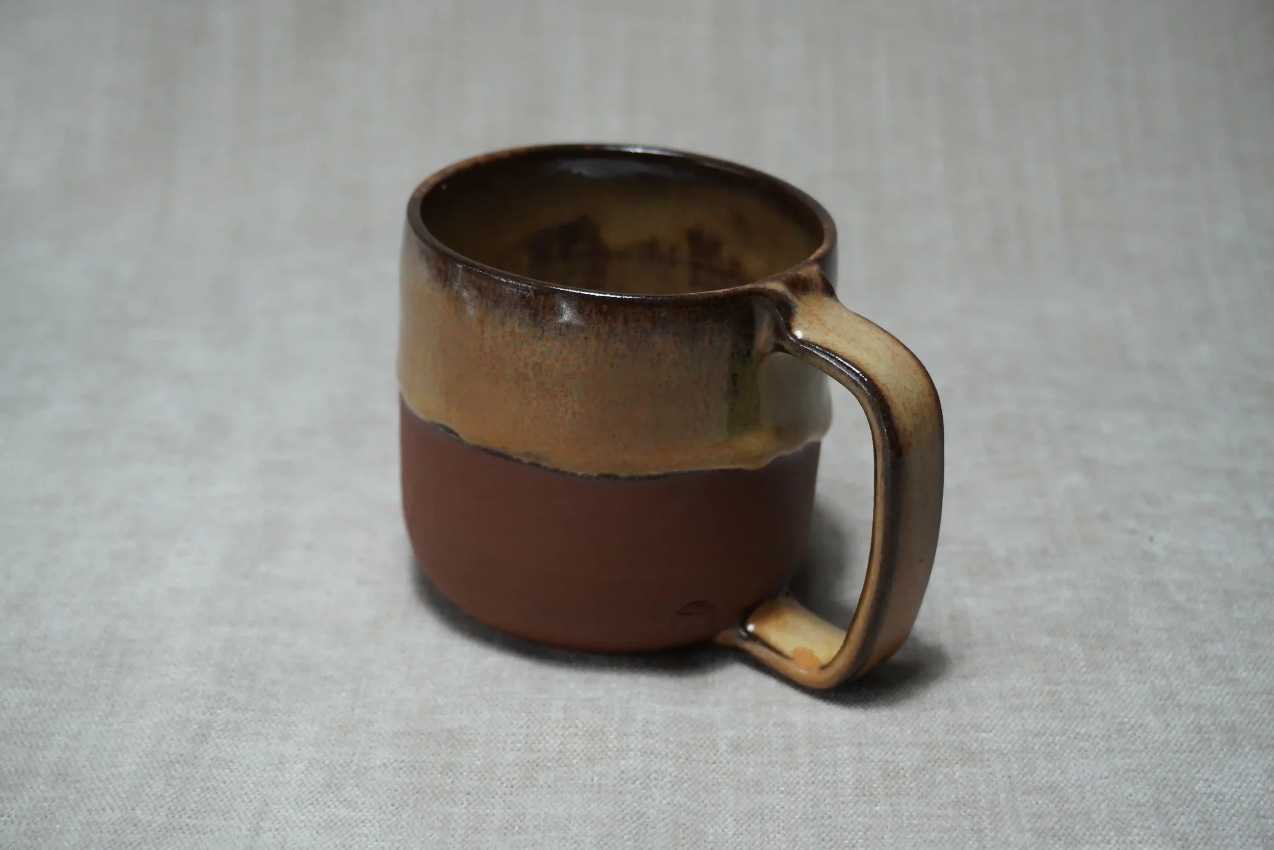 A ceramic mug with a brown and honey-coloured gradient glaze, placed on a light-colored textured surface.