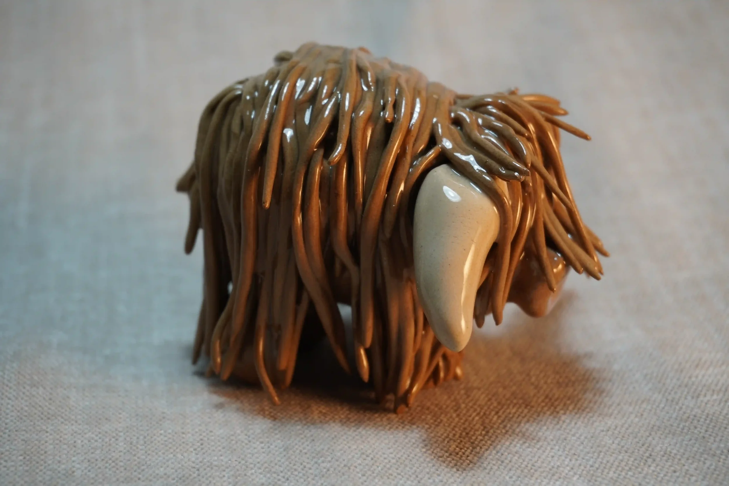 Side view of a cute ceramic pottery Highland Cow ornament made by hand in a milk chocolate colour with beige horns, and placed on a neutral background.