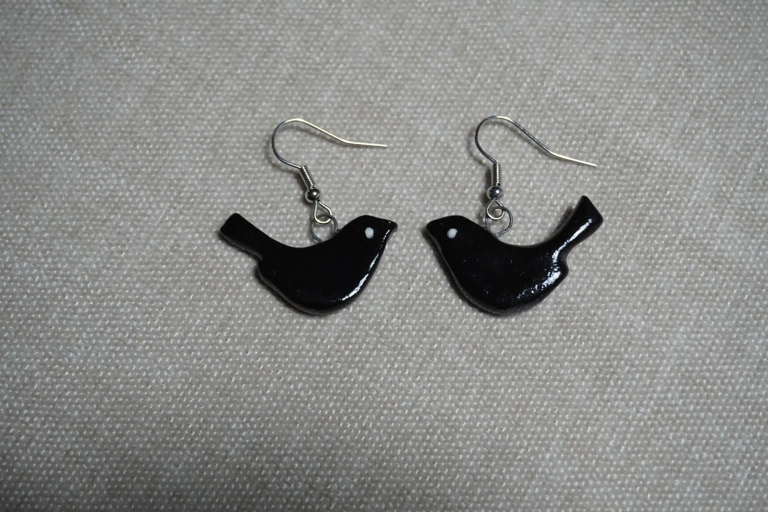 Pair of black bird-shaped earrings with silver hooks lying on a textured light-colored surface.