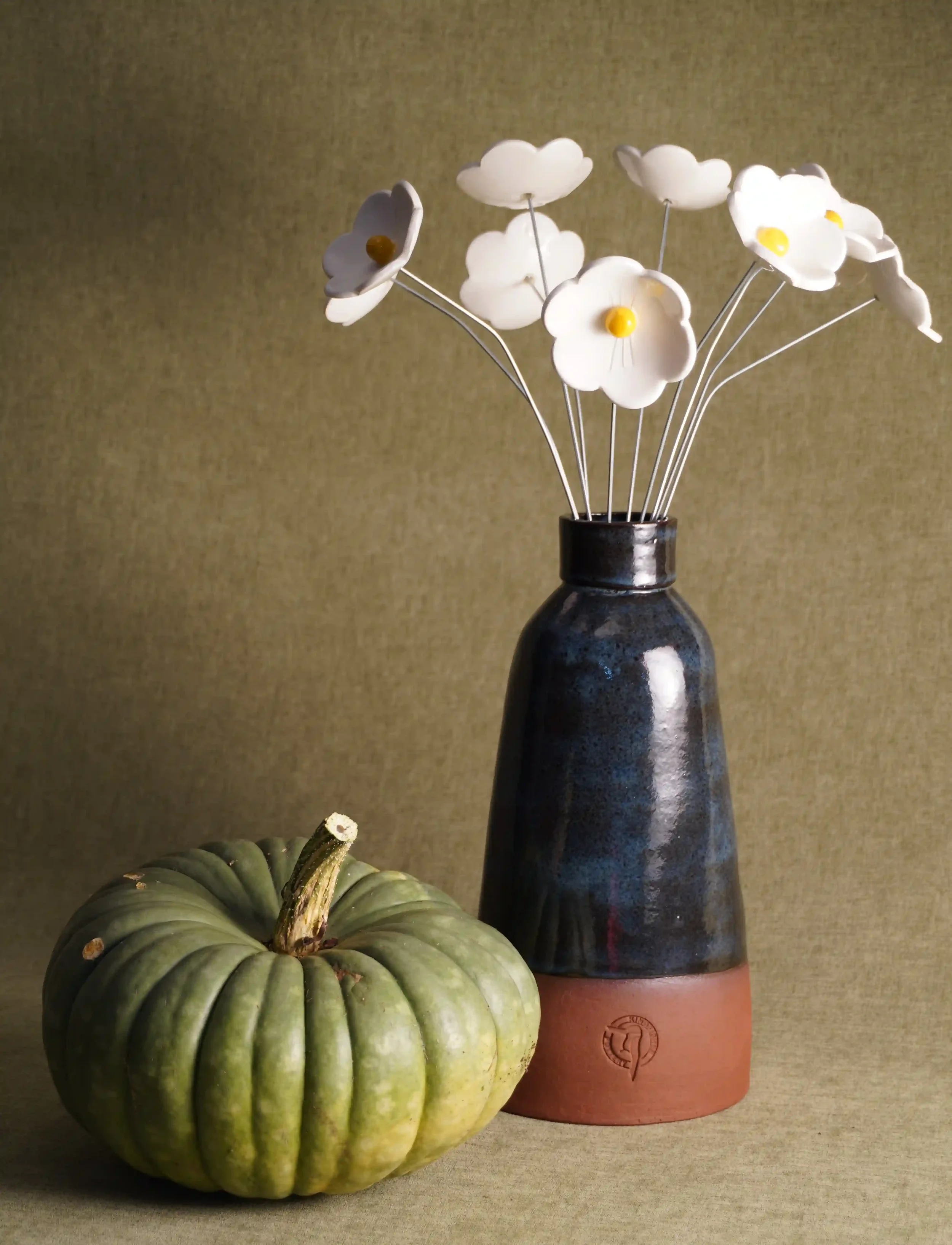A dark blue and terracotta coloured handcrafted pottery vase with ceramic white flowers
