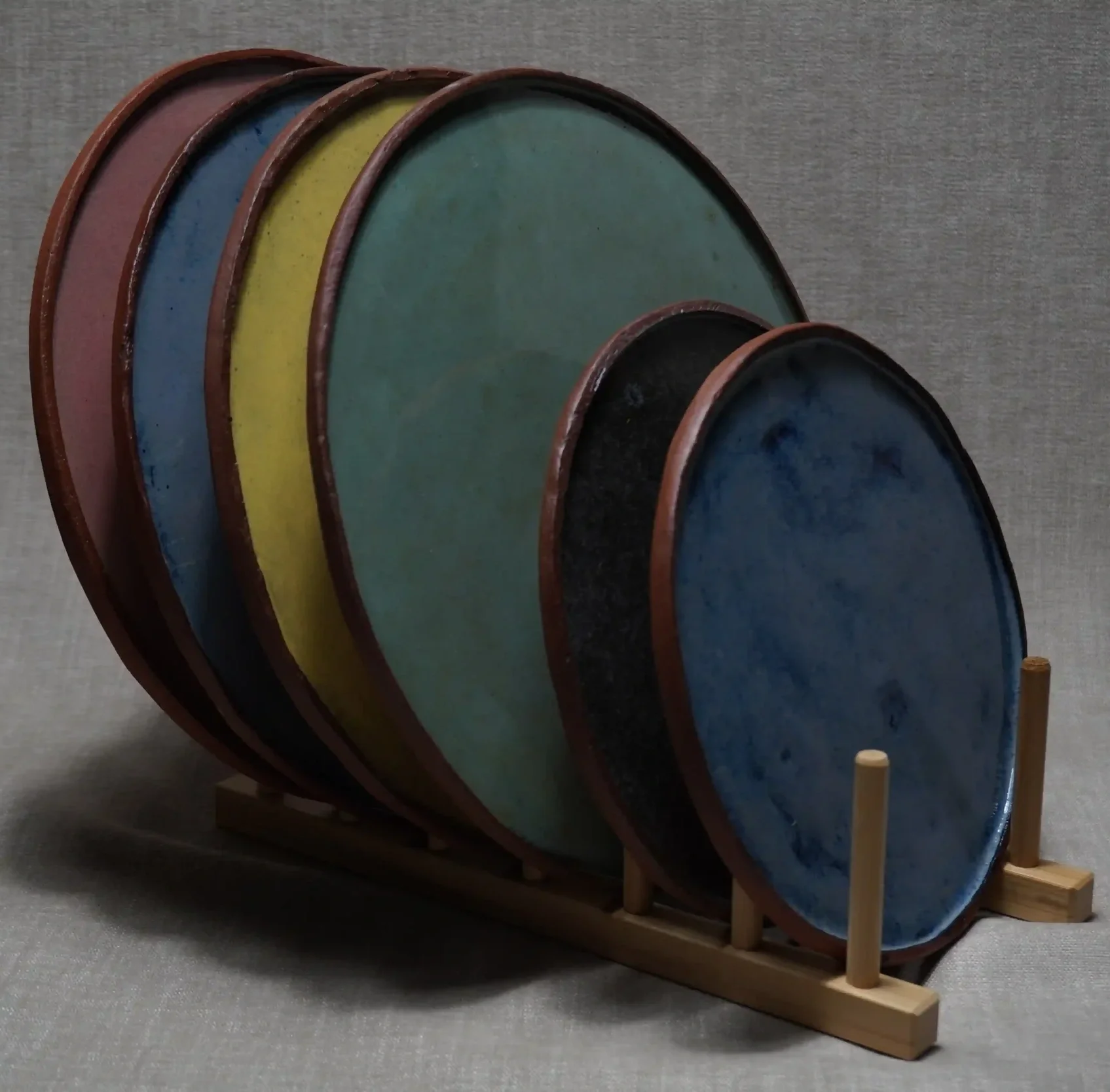 Colorful rustic ceramic pottery plates displayed in a black metal plate rack.