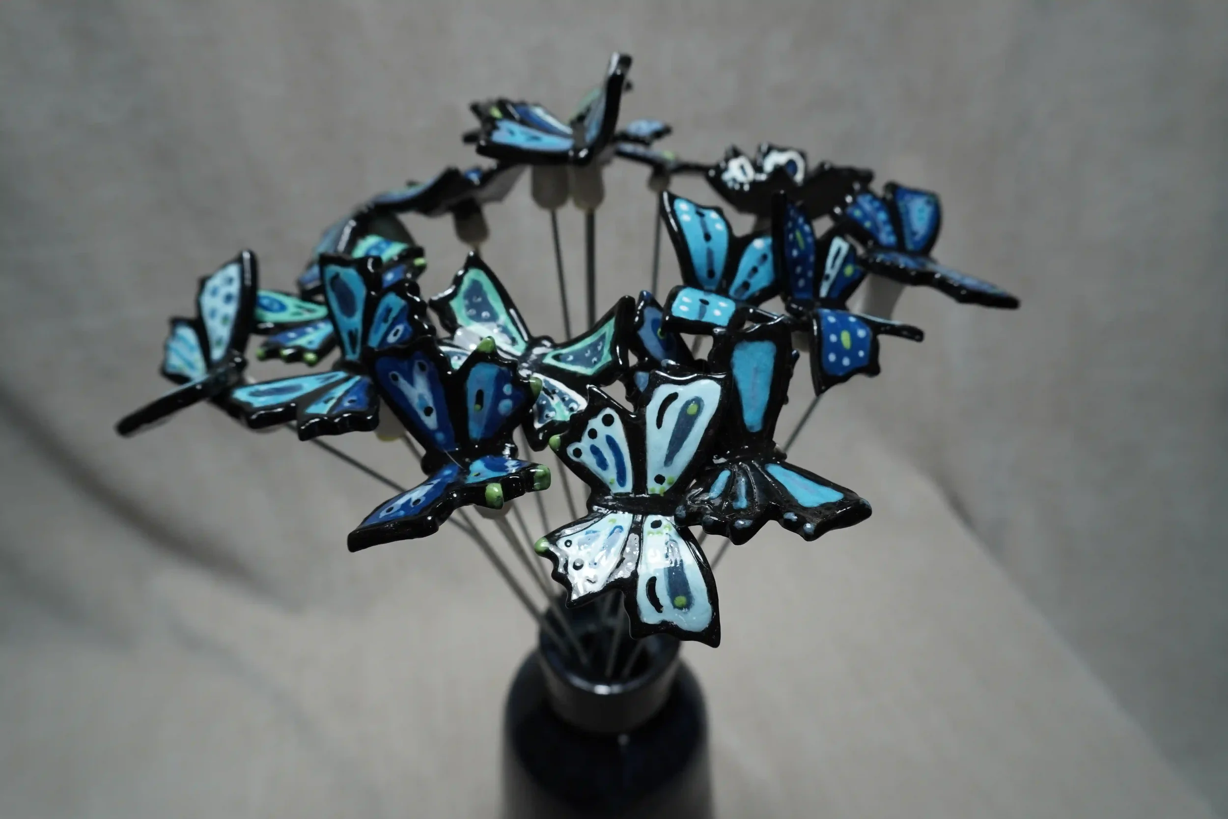 Close-up of a dark blue-glazed ceramic vase holding many ceramic blue butterfly ornaments on metal stems