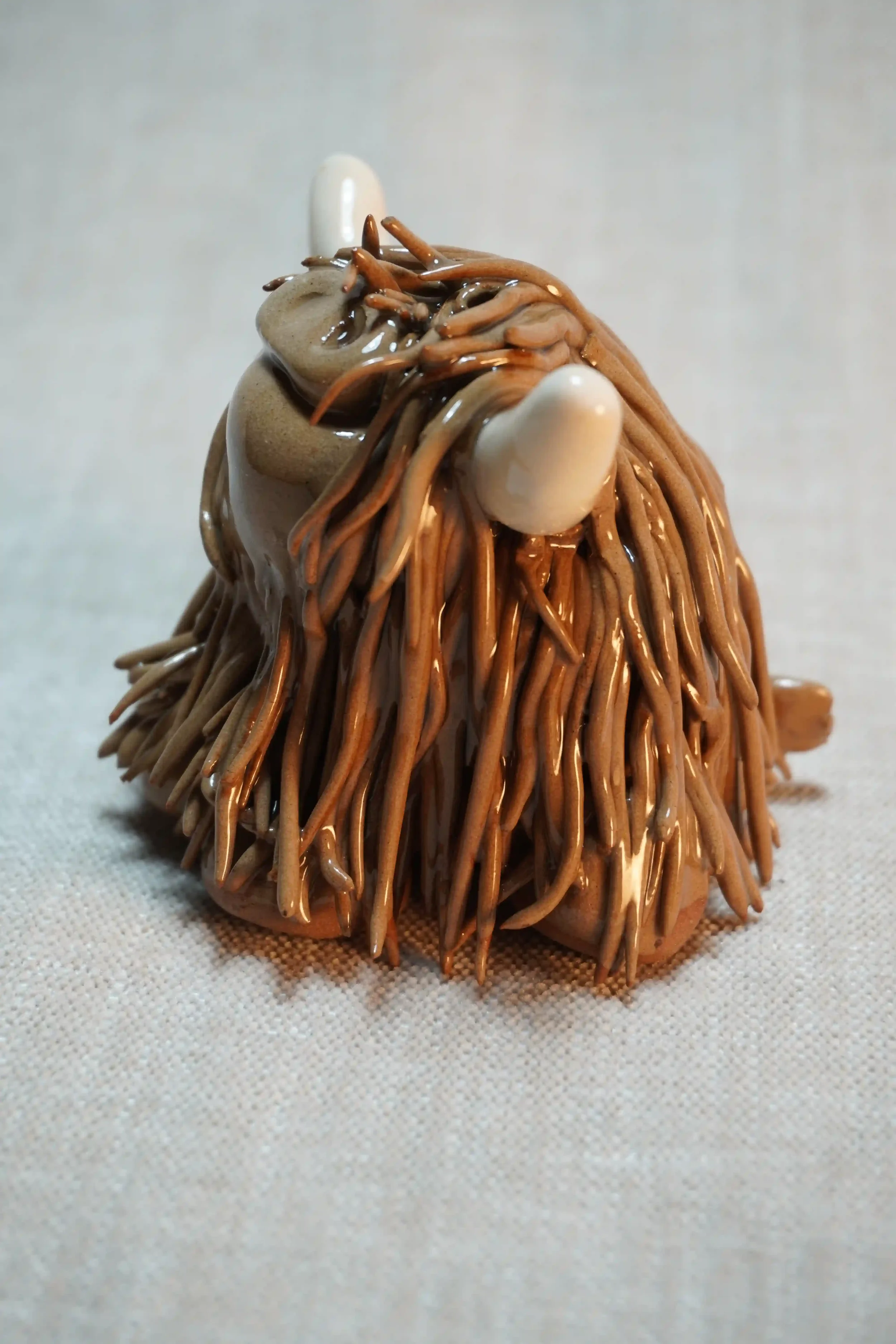 Side view of a handmade ceramic Highland Cow ornament with rich chocolate brown-coloured hair and beige horns.
