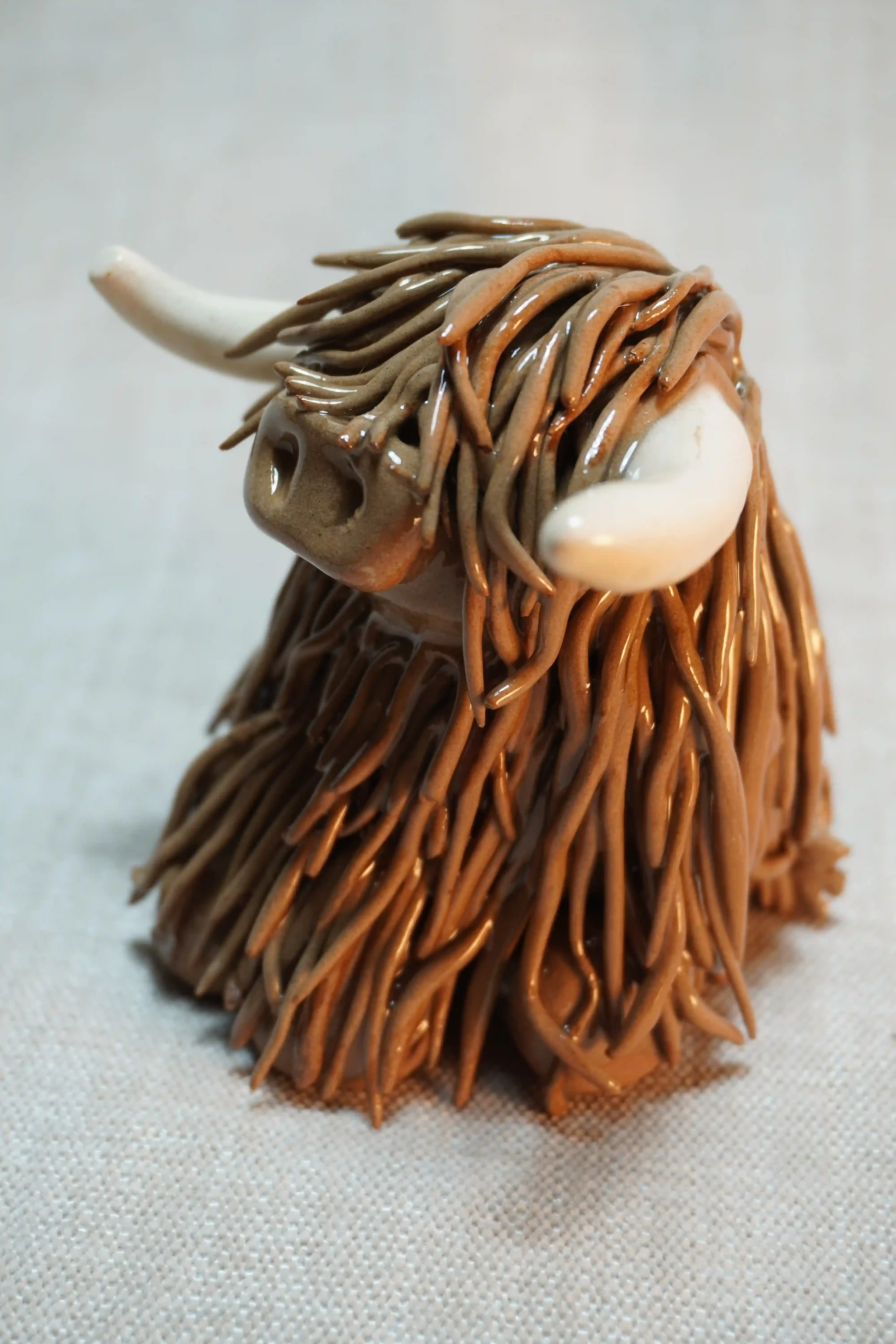 Side view of a ceramic sculpture of a Highland Cow ornament with rich chocolate brown-coloured hair and beige horns.