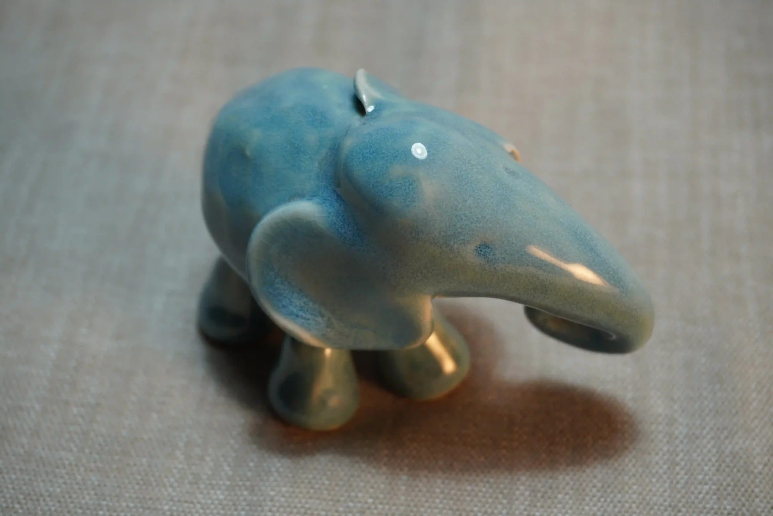 A ceramic figurine of a blue elephant with a glossy finish, displayed on a light-colored surface.