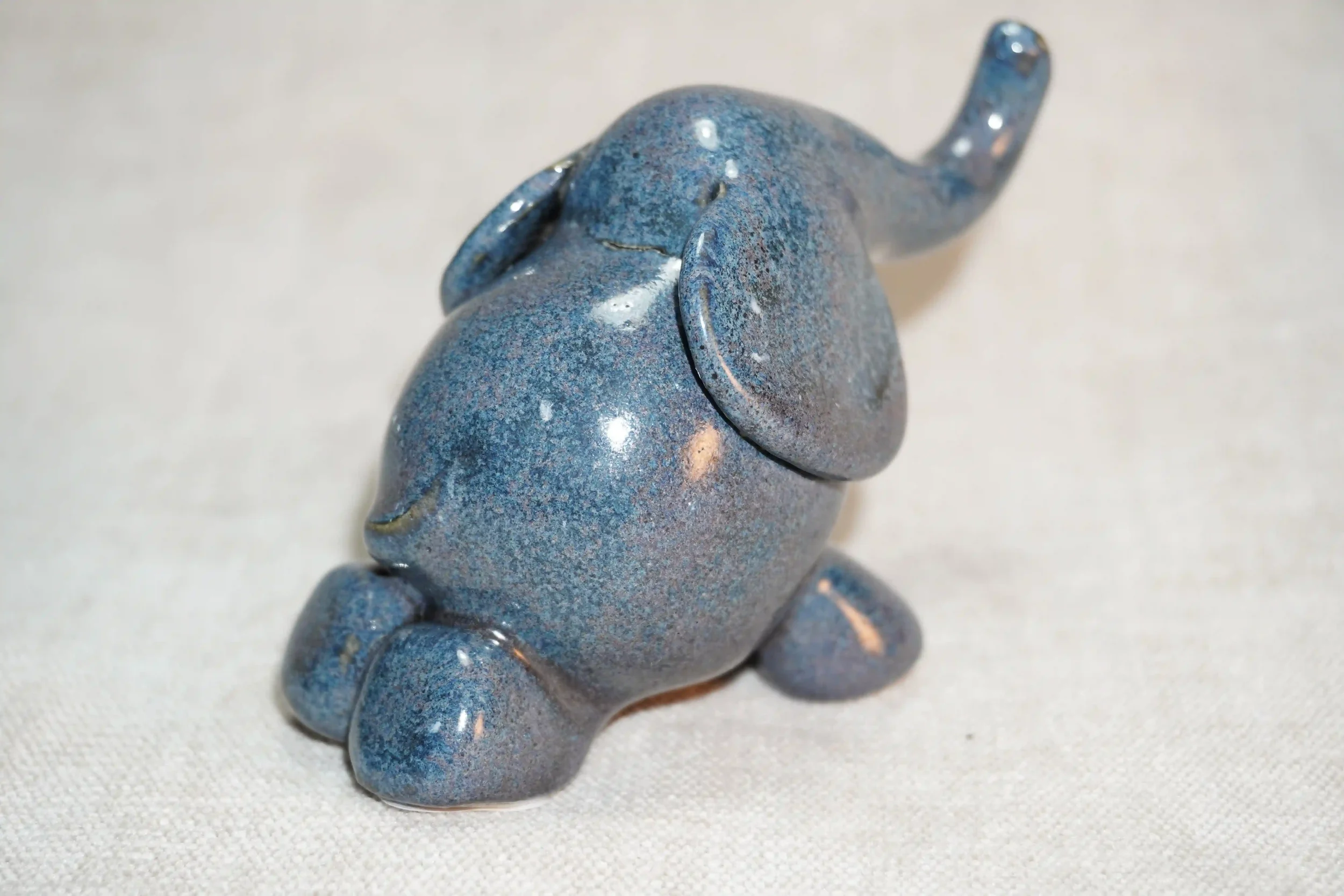 	
	
A small ceramic elephant figurine with a speckled blue glossy glaze finish and it's trunk in the air.