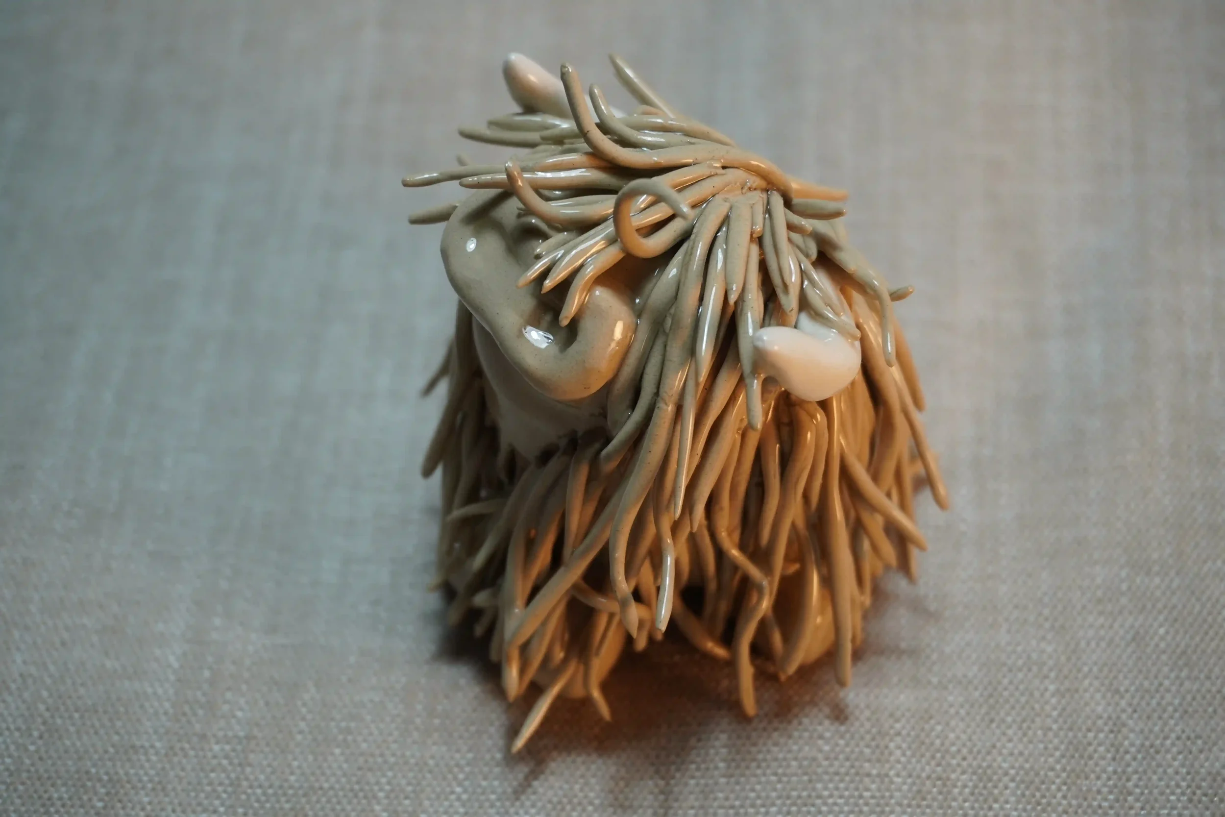 A side view of a cute ceramic sculpture of a Highland Cow with light brown hair and beige horns.