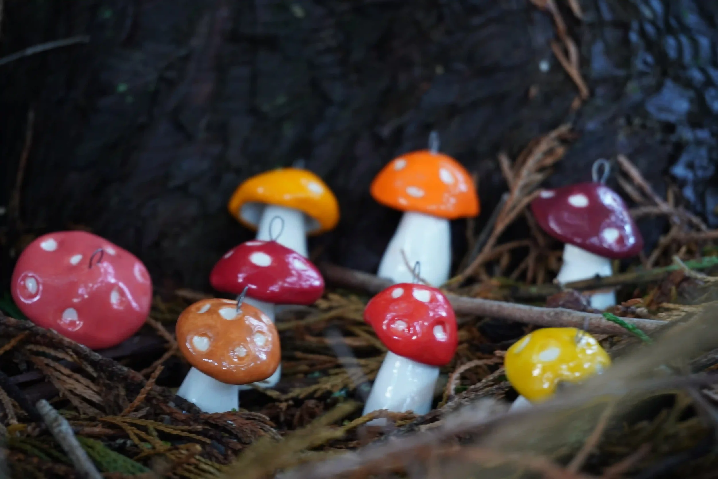 Colorful handmade ceramic mushroom-shaped ornaments displayed with twigs and leaves