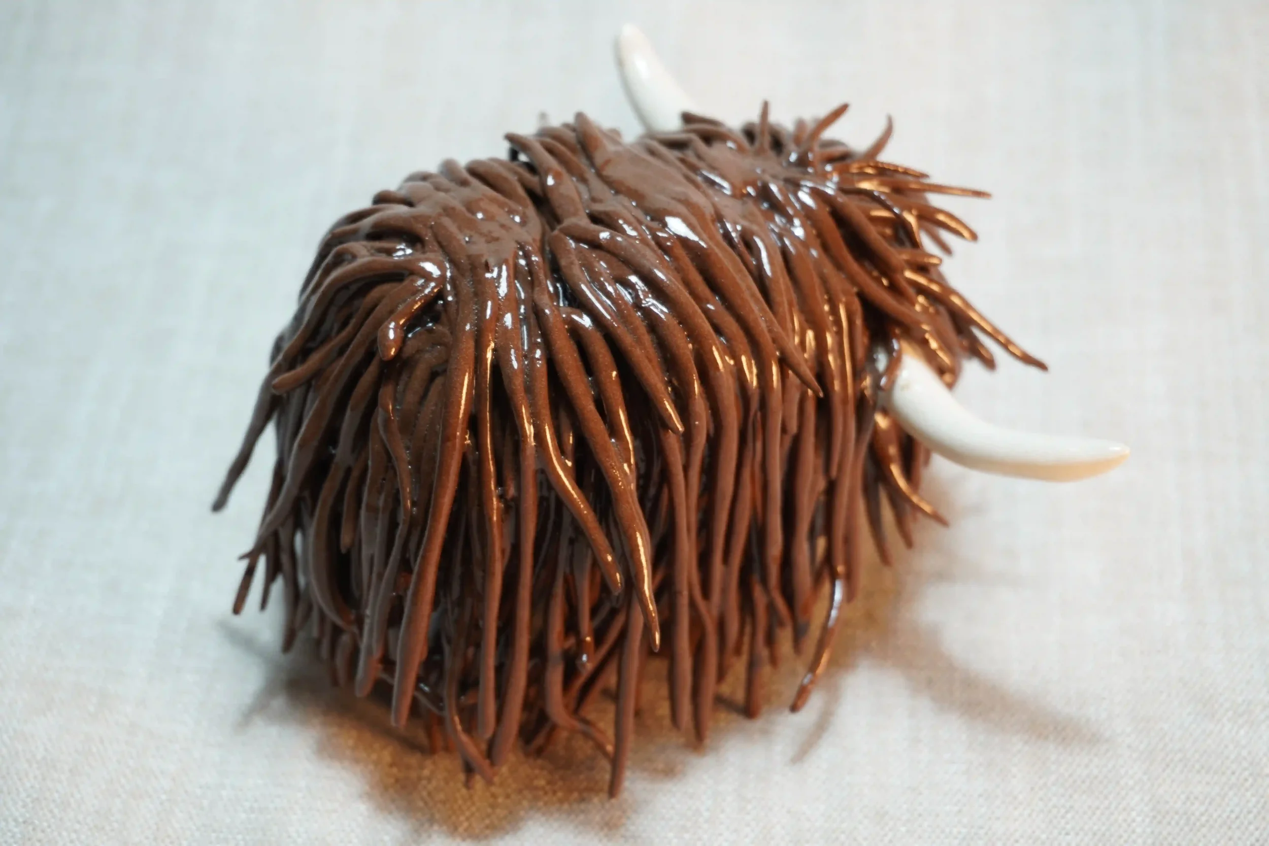 	
Rear view of a handmade pottery ceramic sculpture of a Highland Cow ornament with deep brown-coloured hair and beige horns.