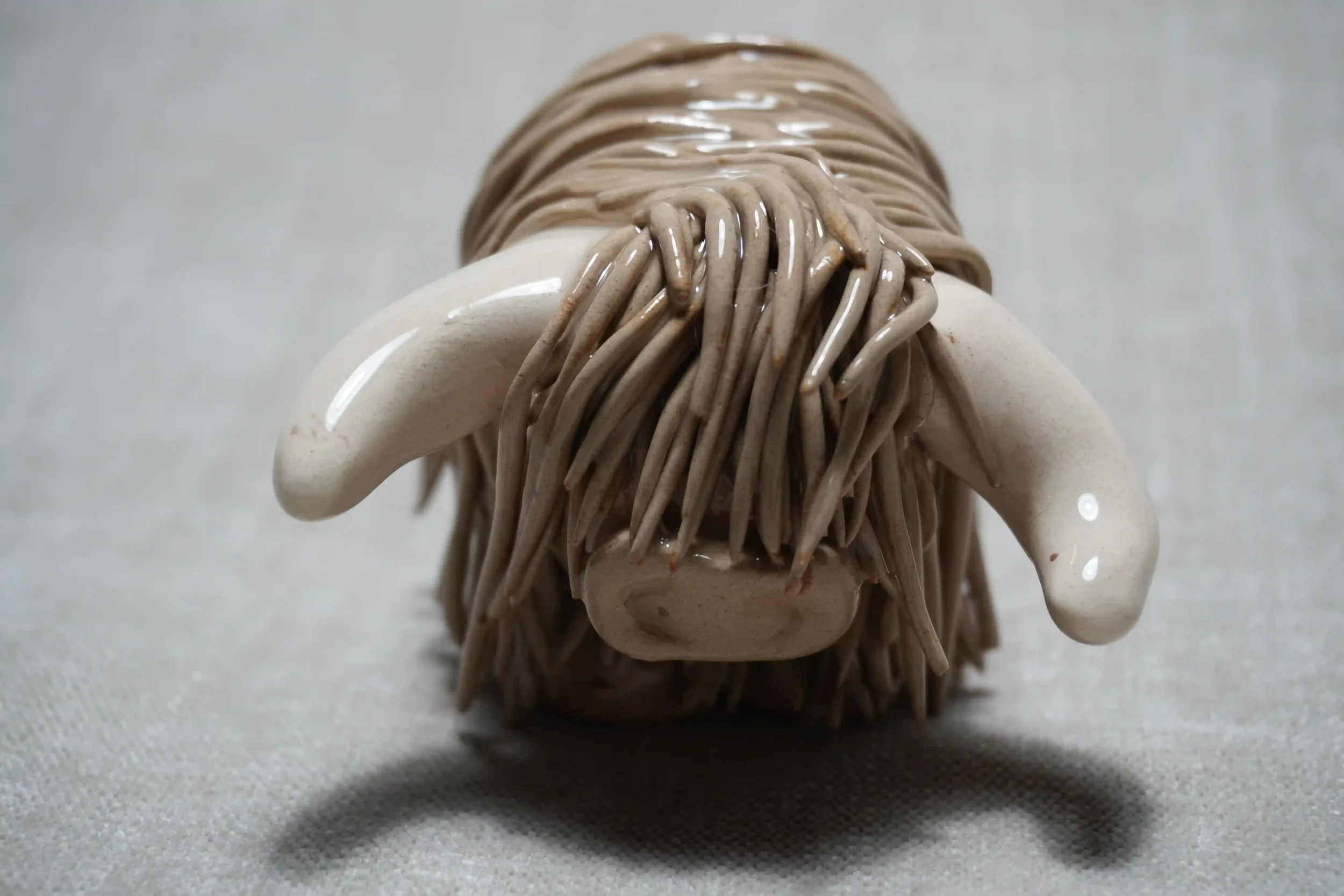 Front view of a cute handmade ceramic Highland Cow ornament with light brown coloured hair and white horns.