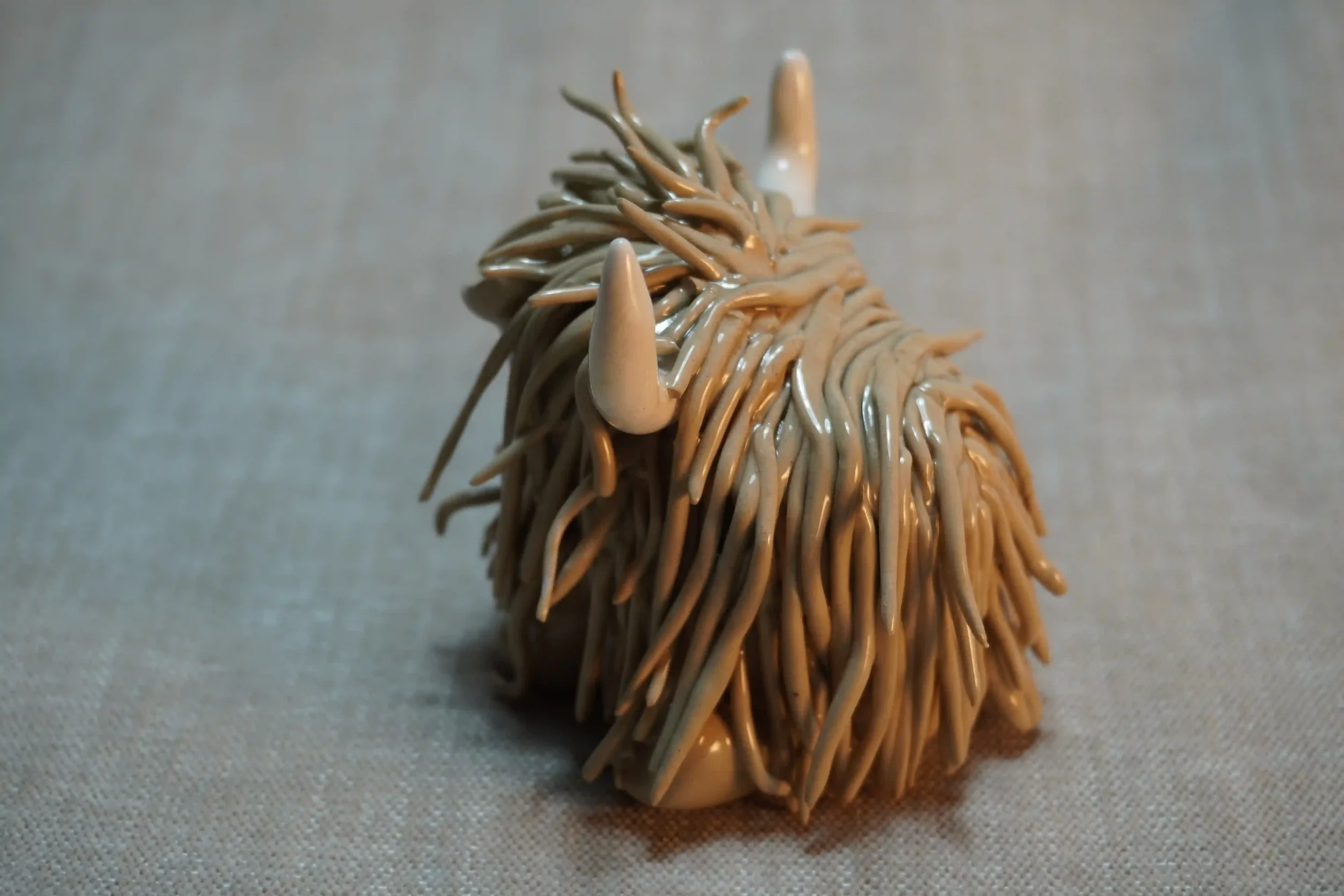 Side view of a ceramic sculpture of a Highland Cow ornament with light brown-coloured hair and curving beige horns.