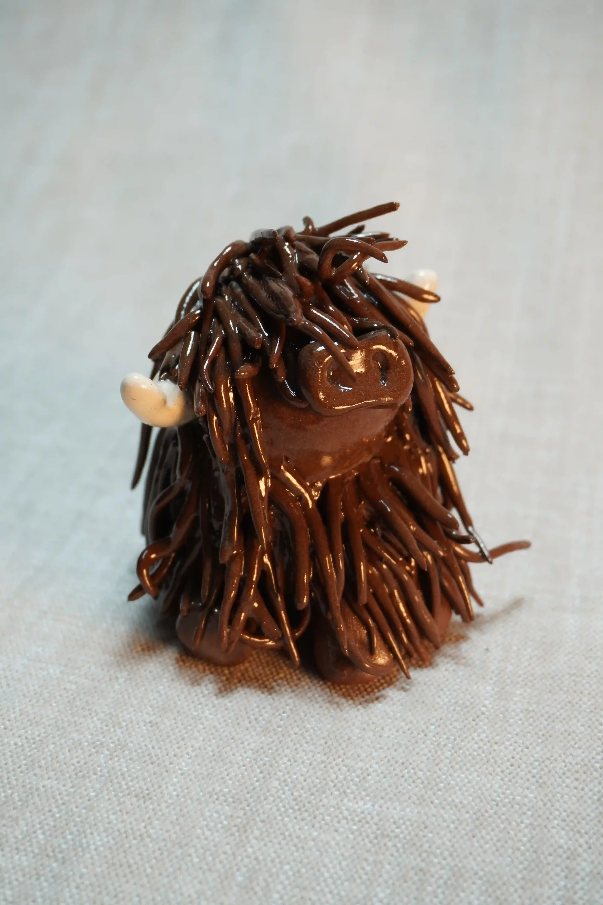 Front view of a ceramic sculpture of a Highland Cow ornament with rich dark brown-coloured hair and beige horns.