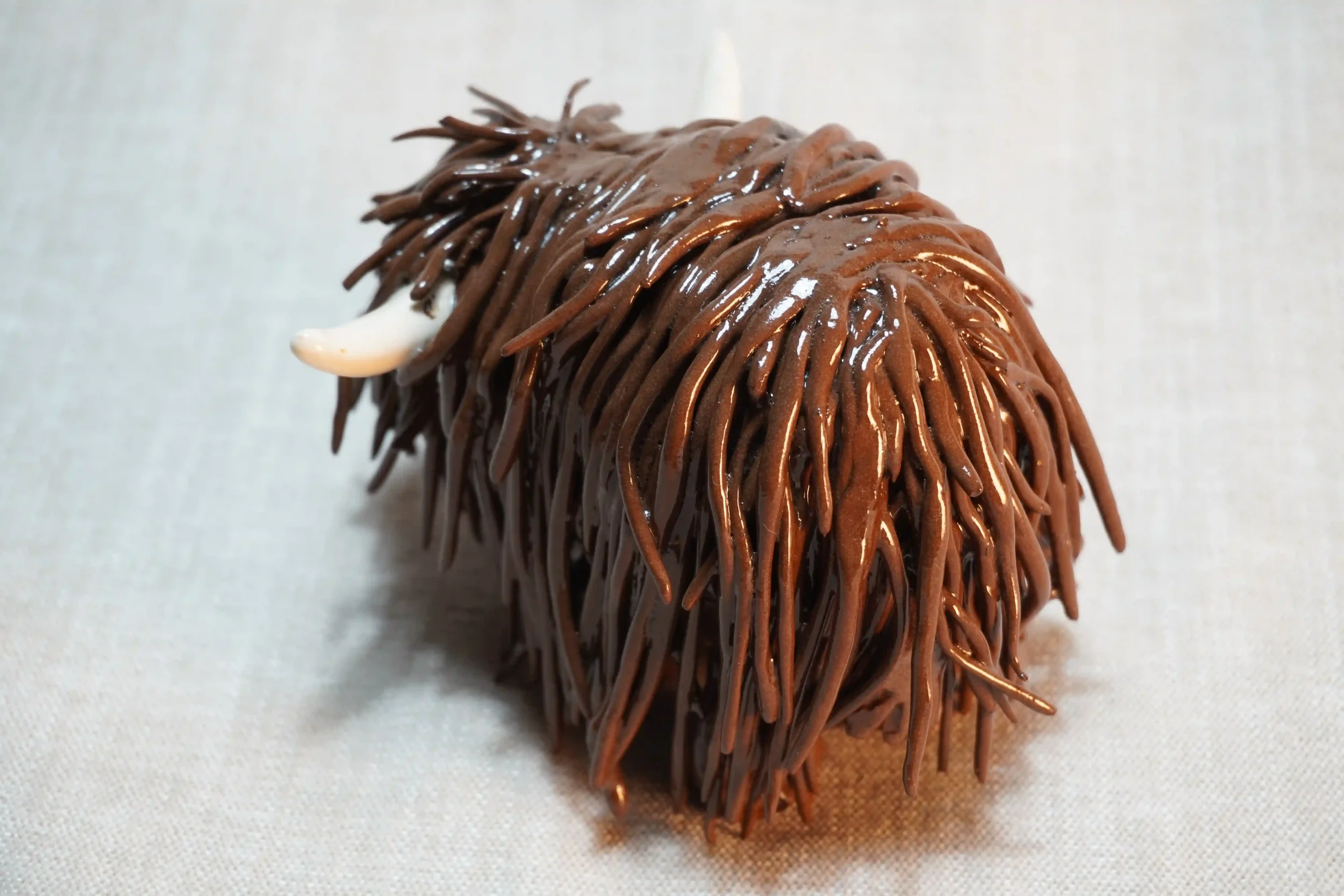	
Rear view of a handmade pottery ceramic sculpture of a Highland Cow ornament with deep brown-coloured hair and beige horns.