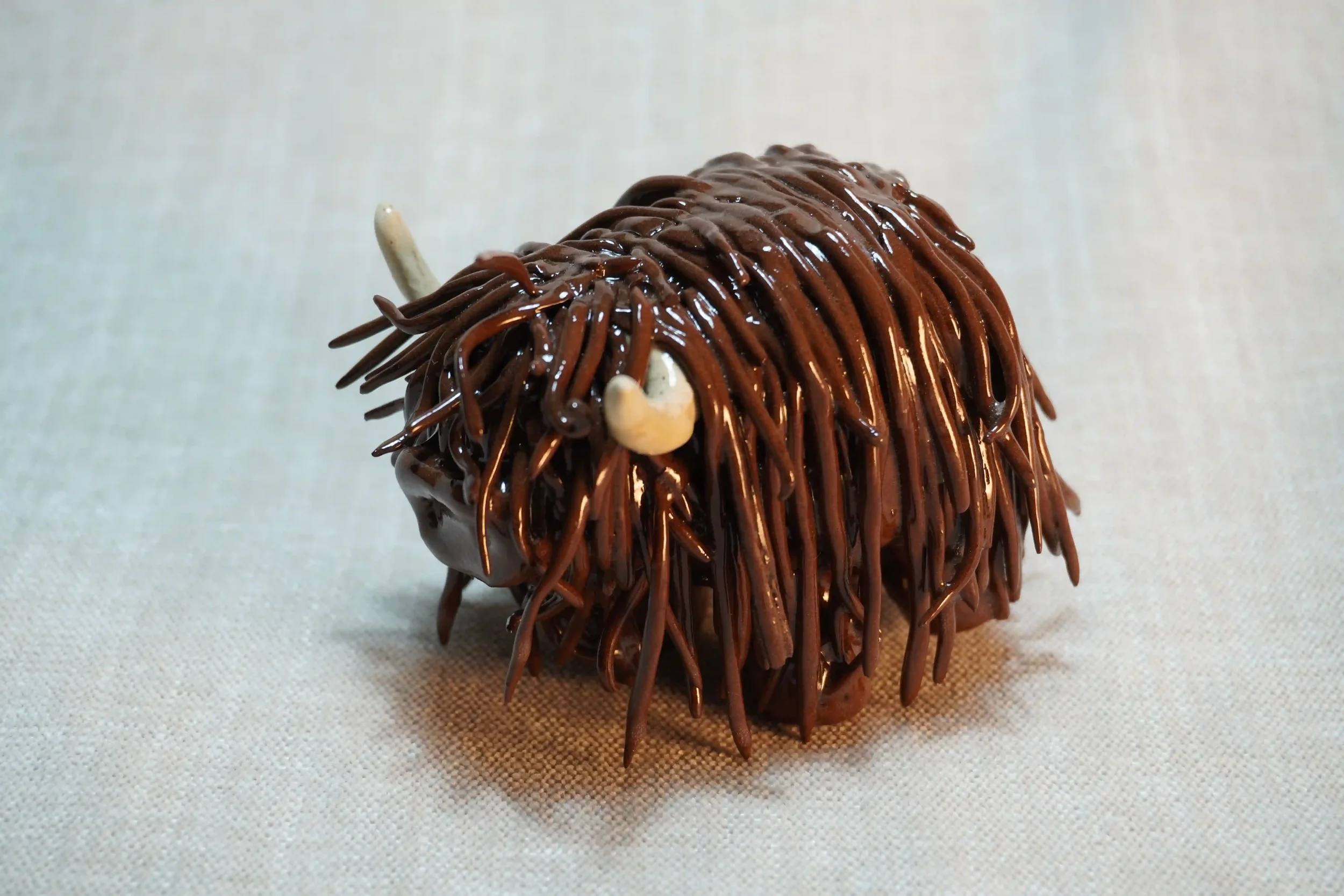 Quarter front view of a ceramic sculpture of a Highland Cow ornament with dark brown-coloured hair and beige horns.