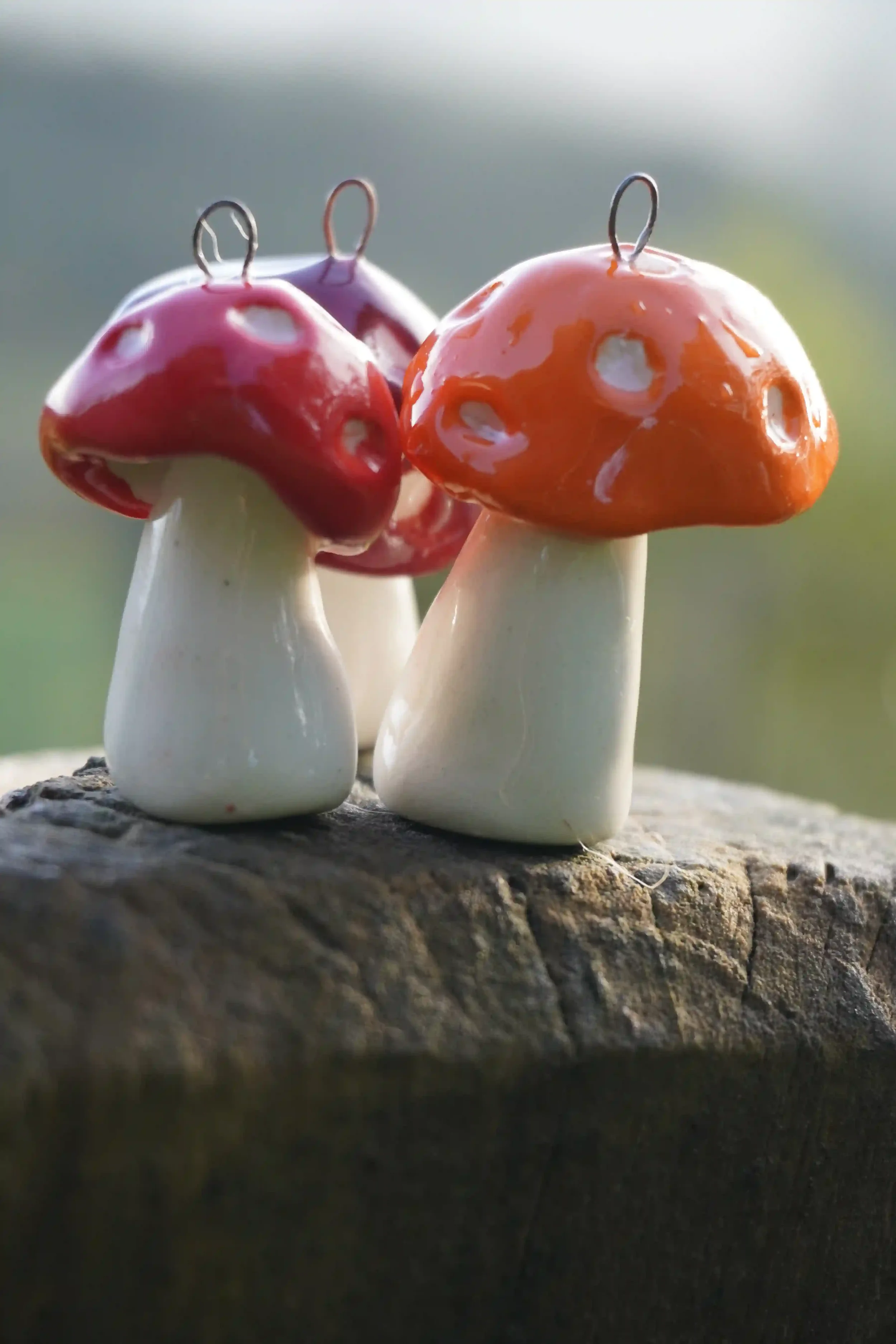 Three ceramic mushroom figurines with glossy red and orange caps and white stems on a rough wooden surface, blurred background.