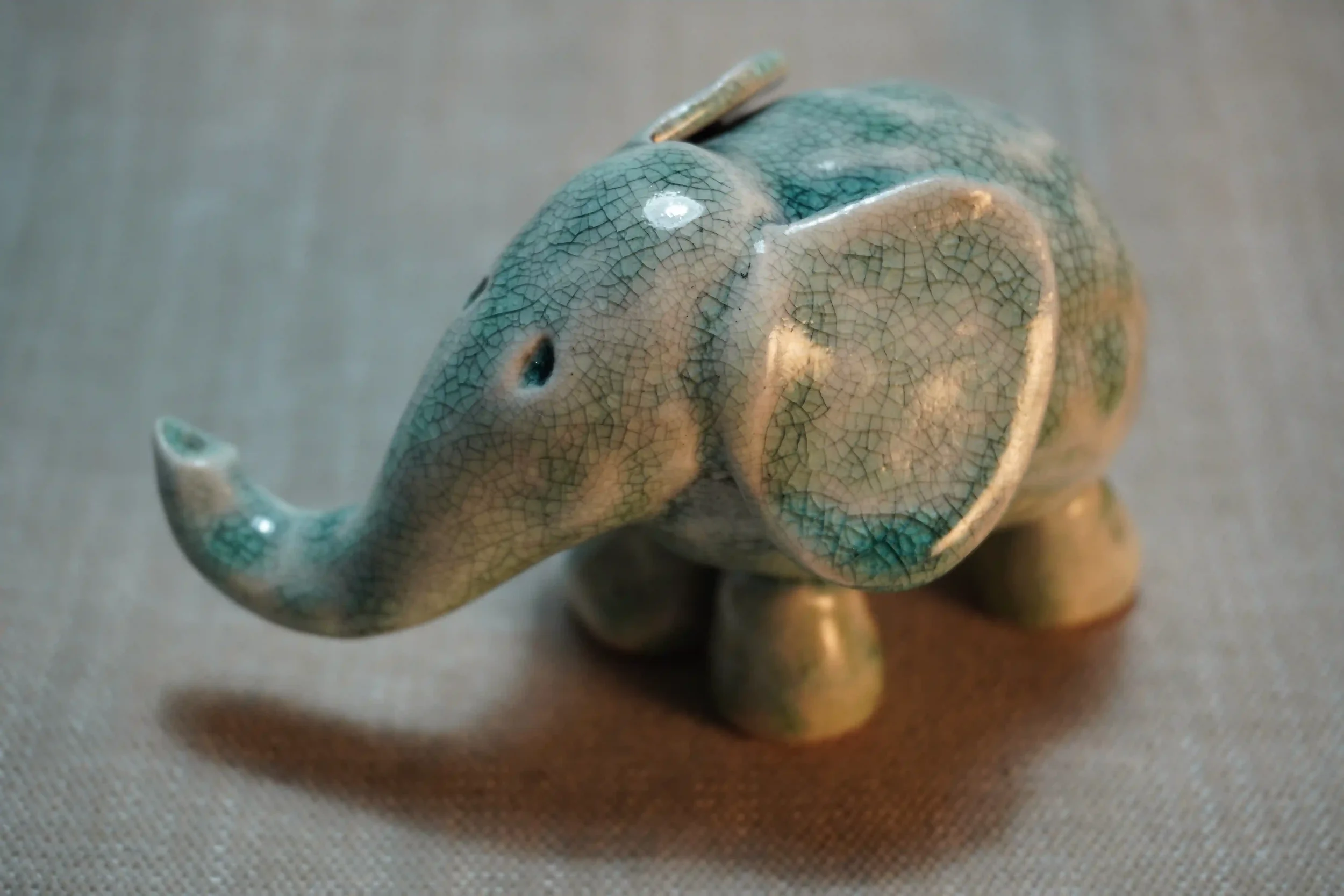 Small handmade ceramic elephant figurine with a crackled turquoise glaze finish placed on a gray surface.