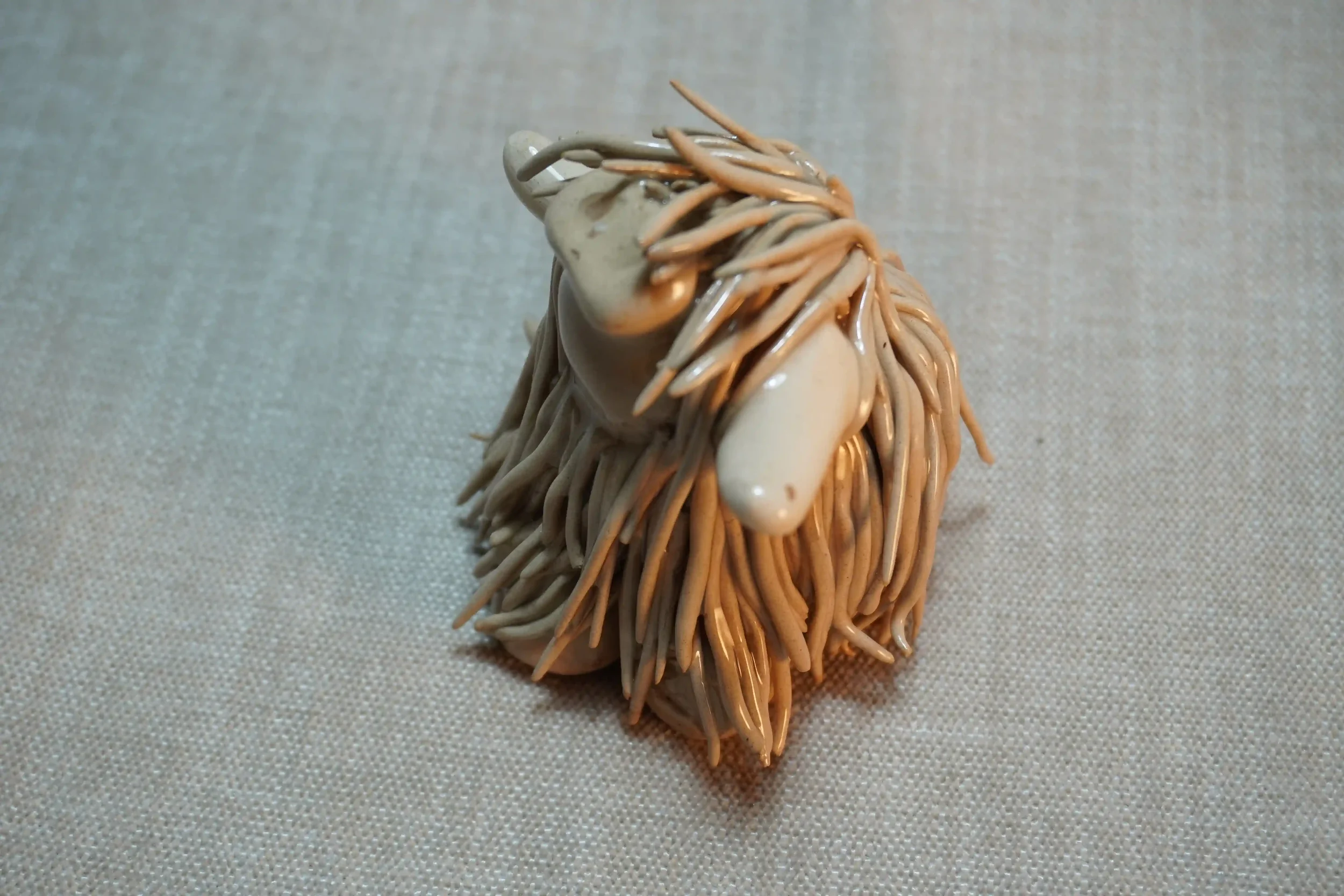 Side view of a handmade ceramic sculpture of a Highland Cow ornament with light tan-coloured hair and beige horns.